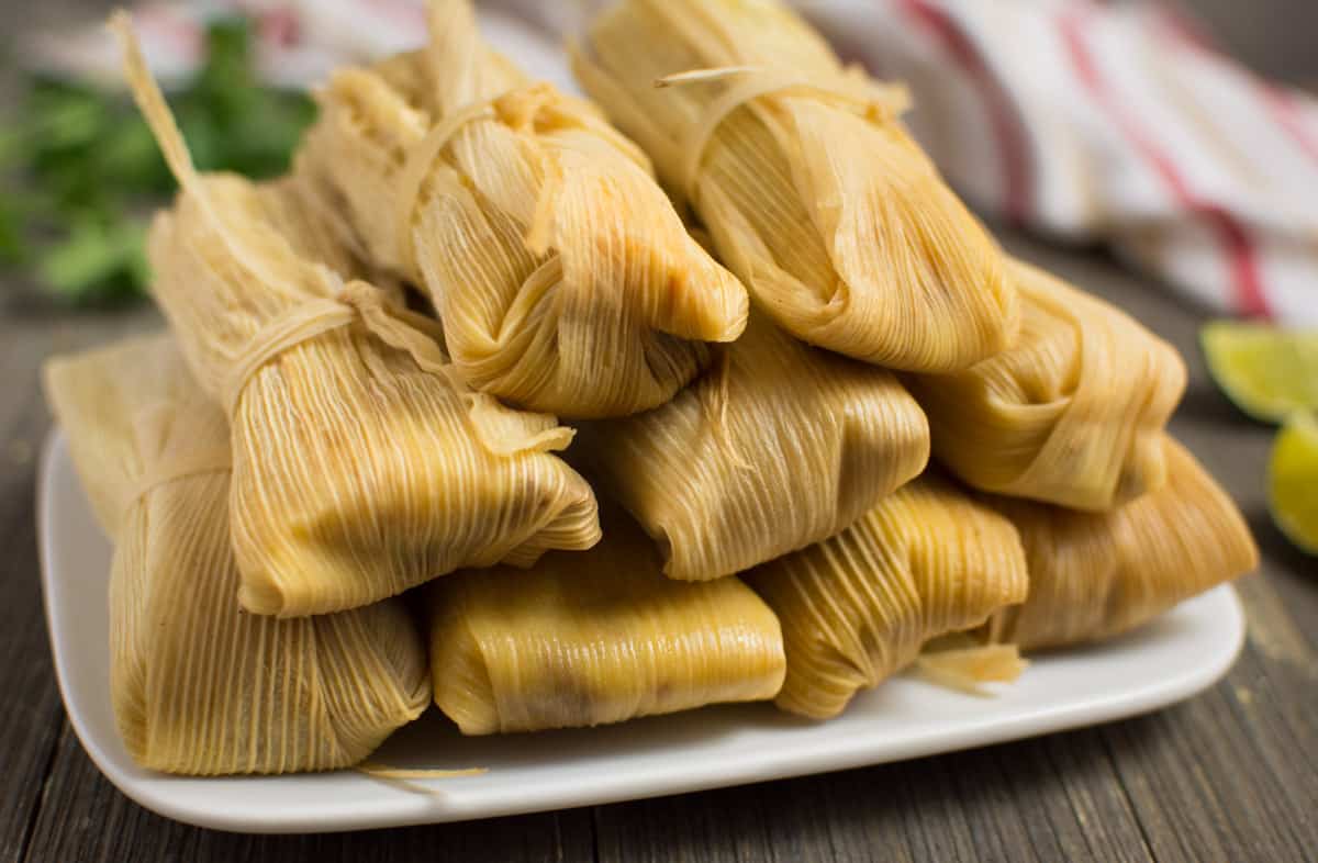 Vegan tamales wrapped in corn husks stacked on a plate.