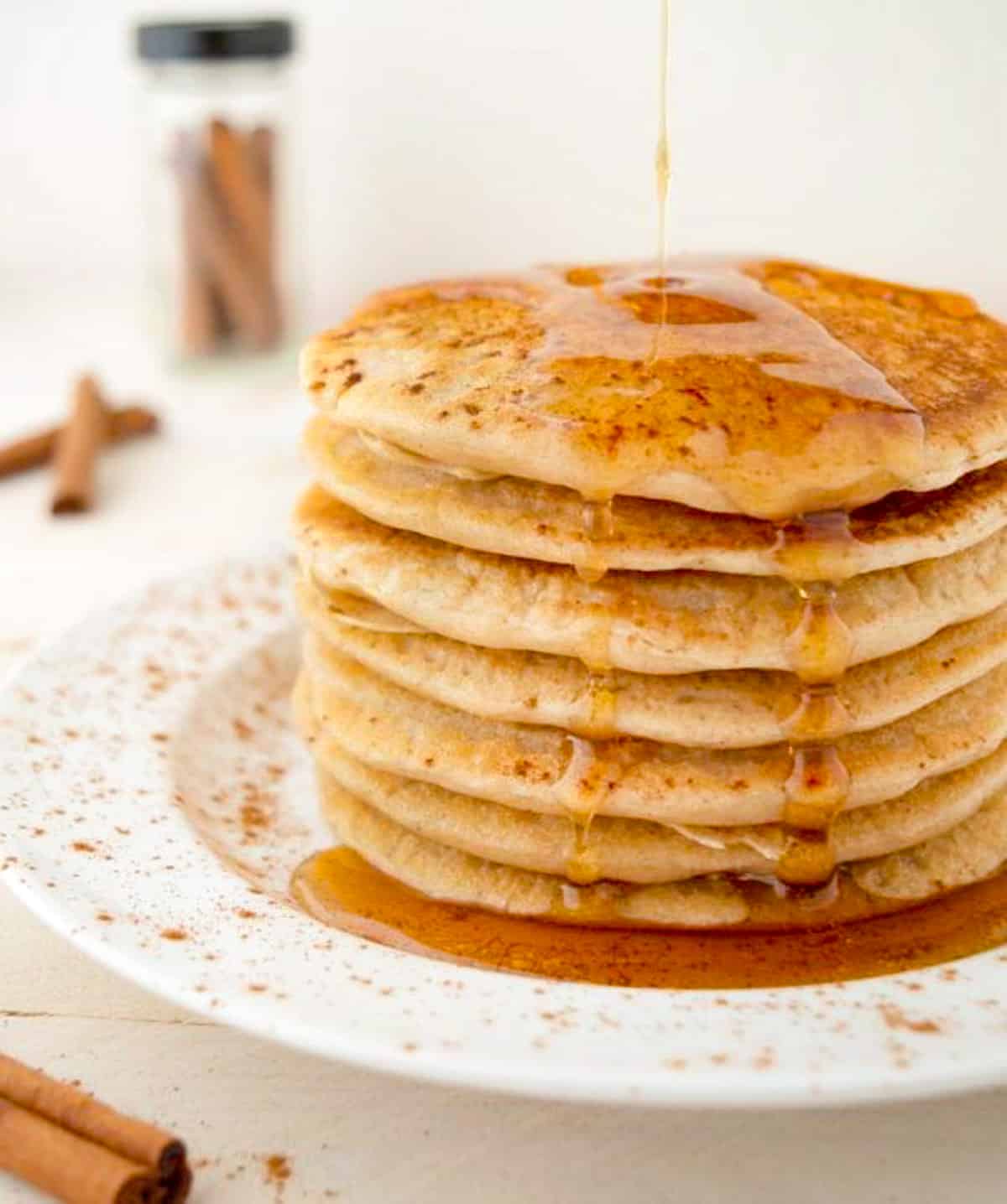 Maple syrup being drizzled onto a stack of vegan cinnamon pancakes.