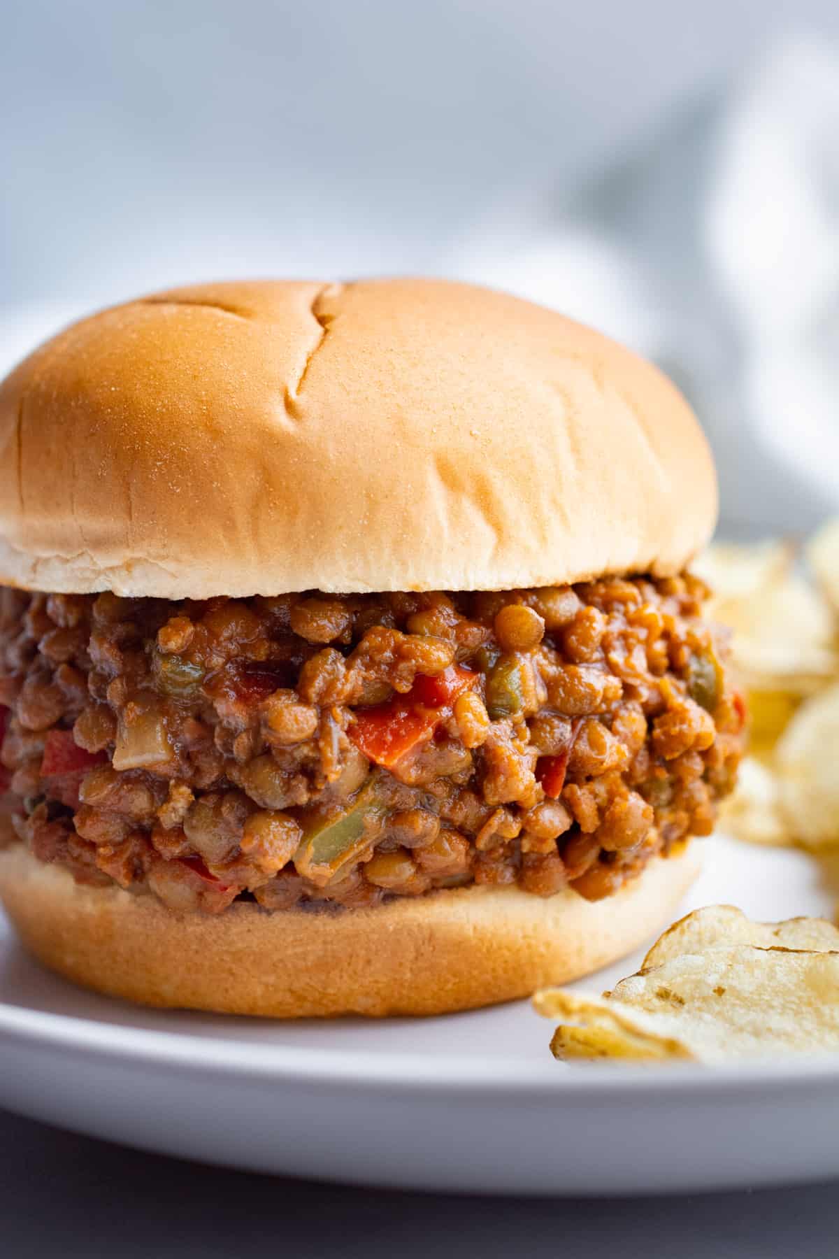 vegan lentil and tofu sloppy joes on a white bun with a side of potato chips.