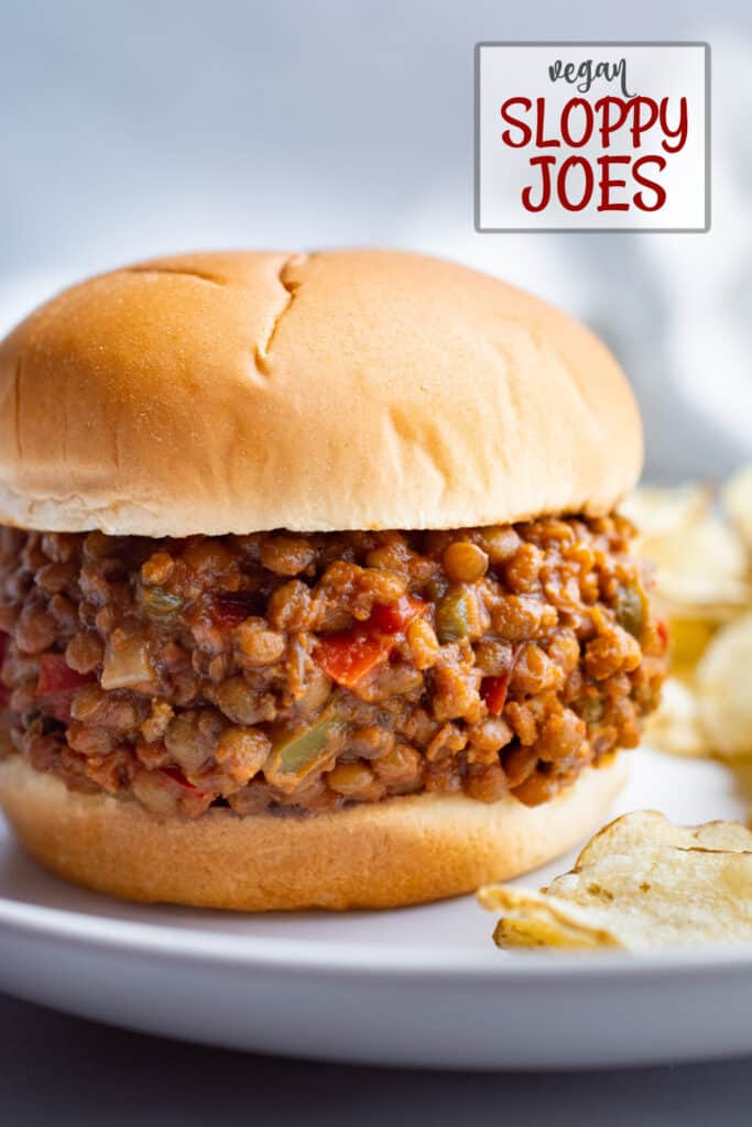 Vegan lentil sloppy joe on a white bun with potato chips on the side.