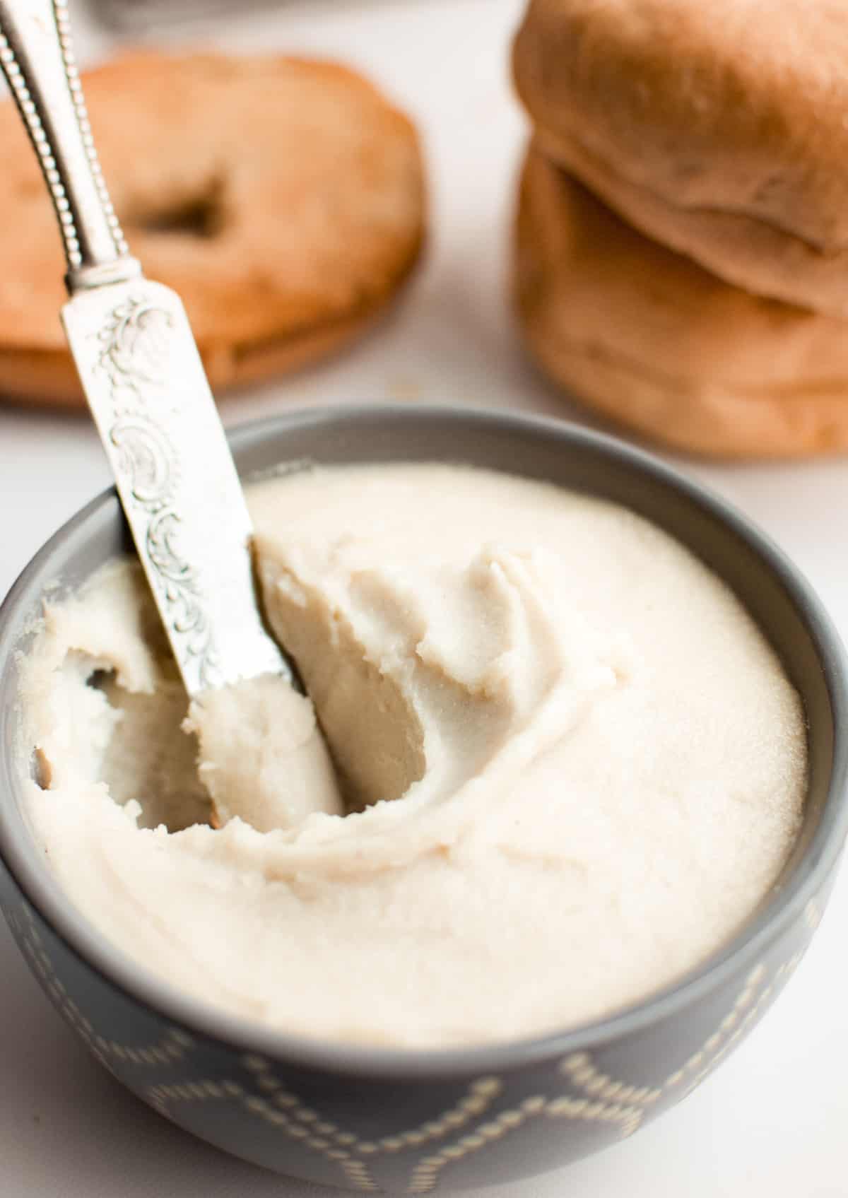 A small gray bowl filled with cashew cream cheese and a knife digging into it.