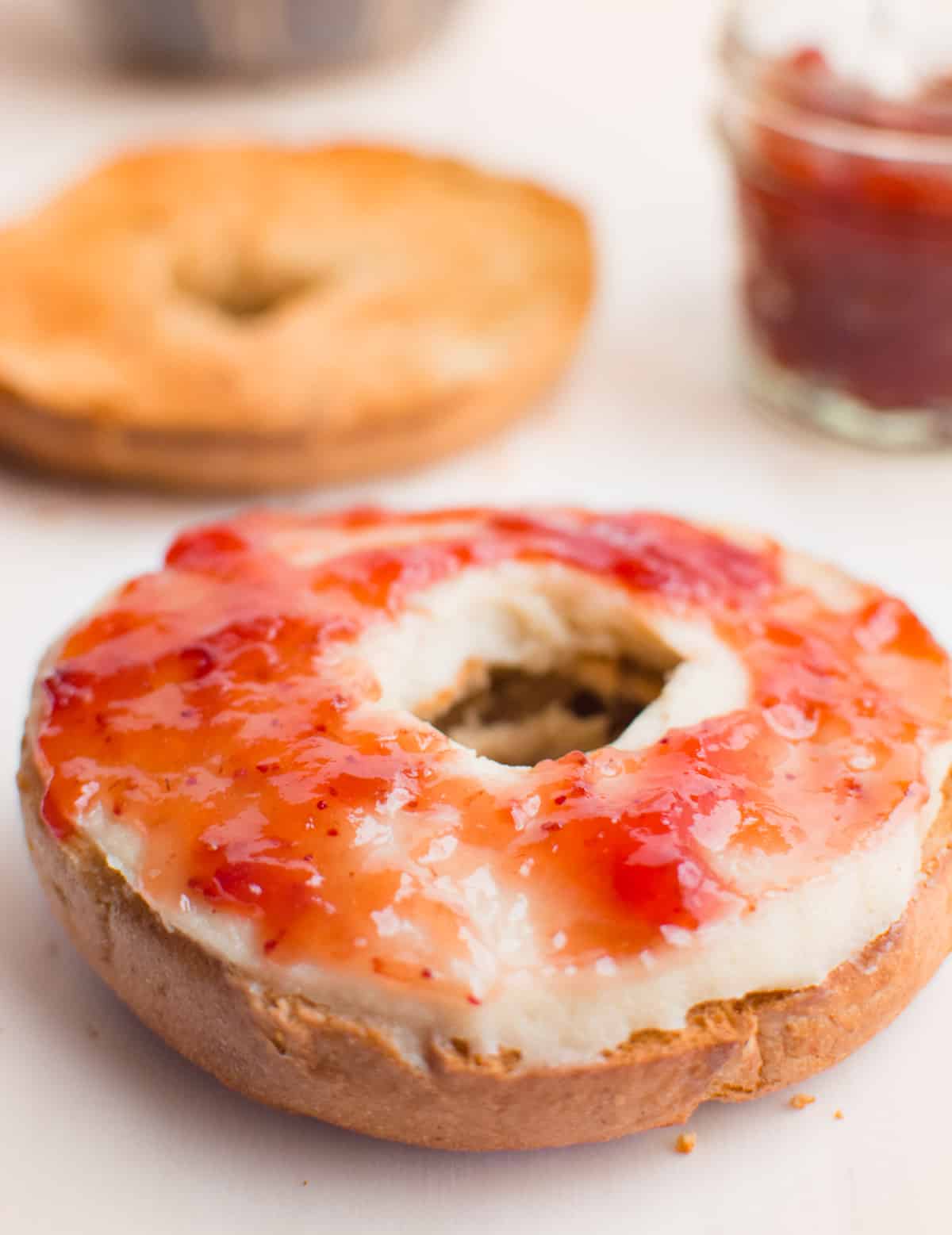 A toasted bagel spread with cashew cream cheese and strawberry preserves.