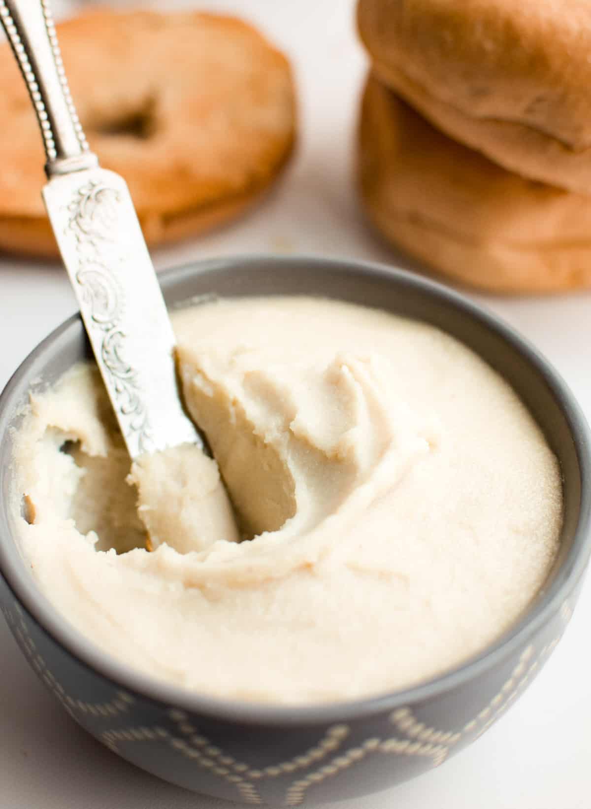 A small gray bowl filled with cashew cream cheese and a knife digging into it.
