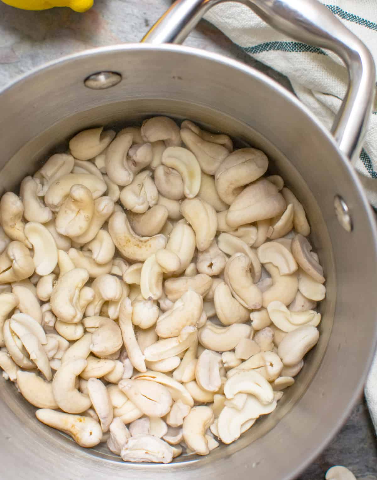 A stainless steel saucepan with cashews soaking in hot water.