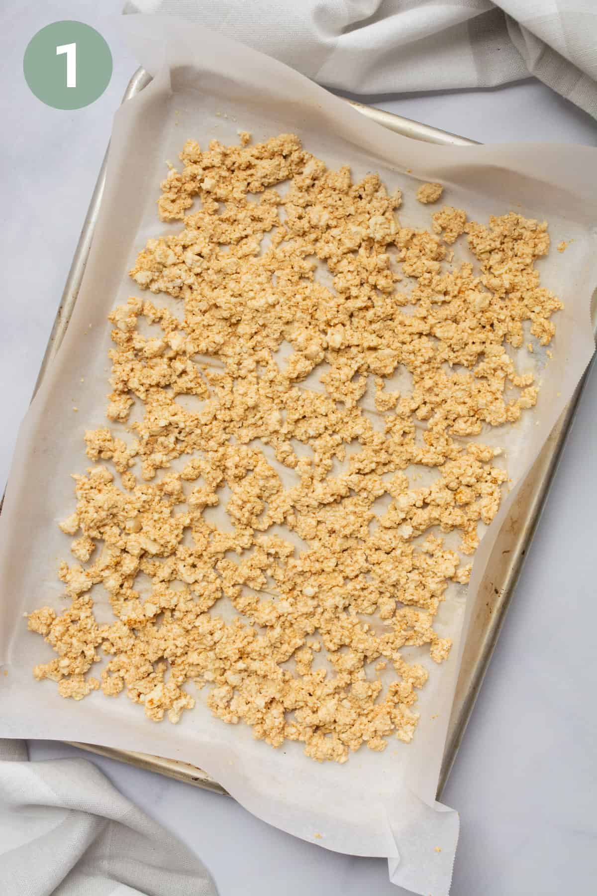 Crumbled tofu on a baking sheet lined with parchment paper.