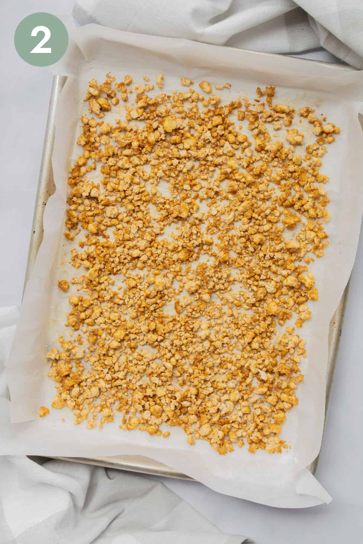 Crumbled tofu on a baking sheet with parchment paper after being baked.