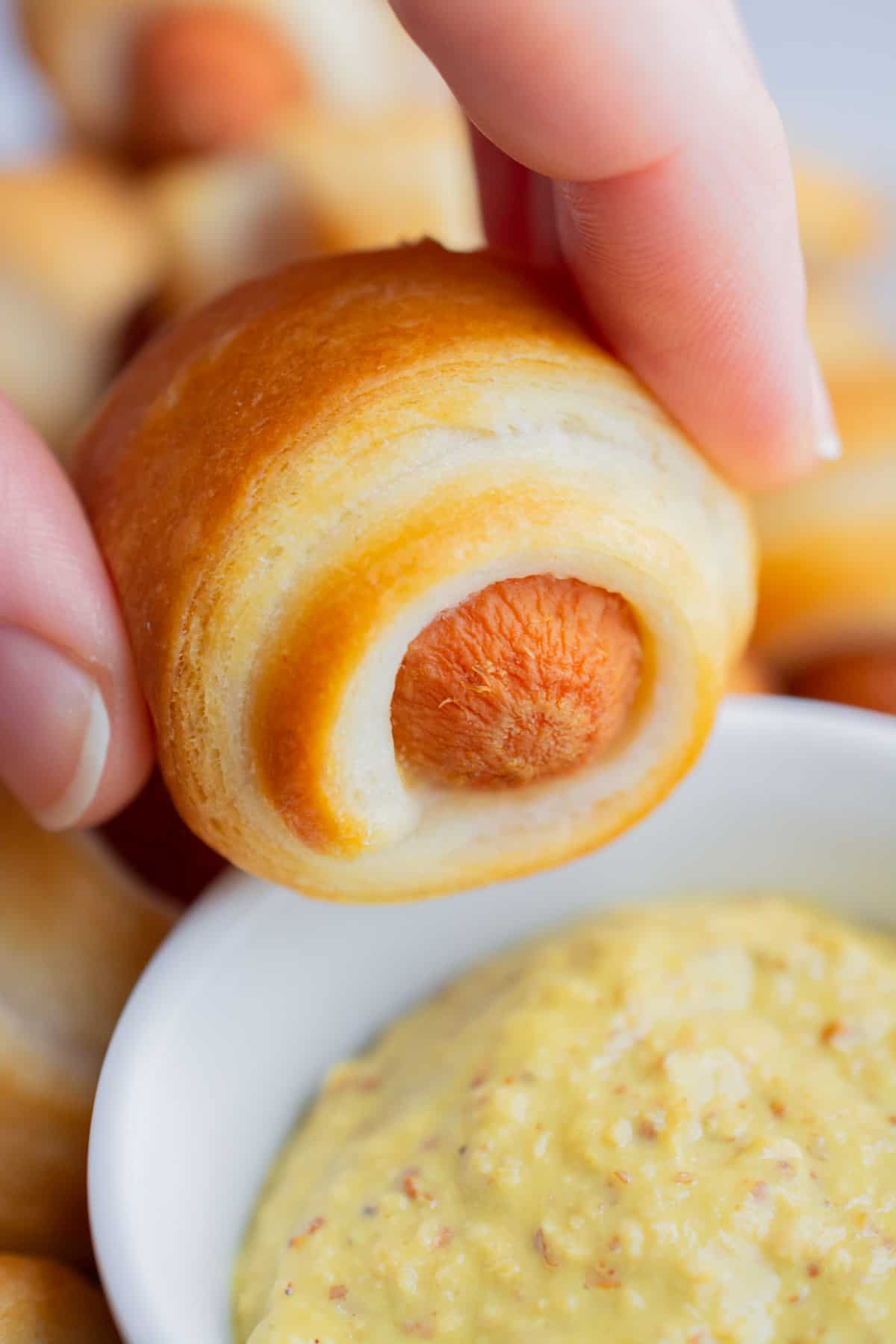 Two fingers holding a mini vegan crescent dog ready to dip it in mustard.
