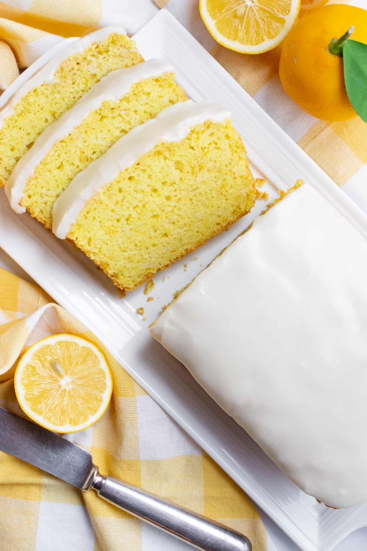 Vegan lemon bread topped with lemon icing on a white serving plate and three slices cut from it. 