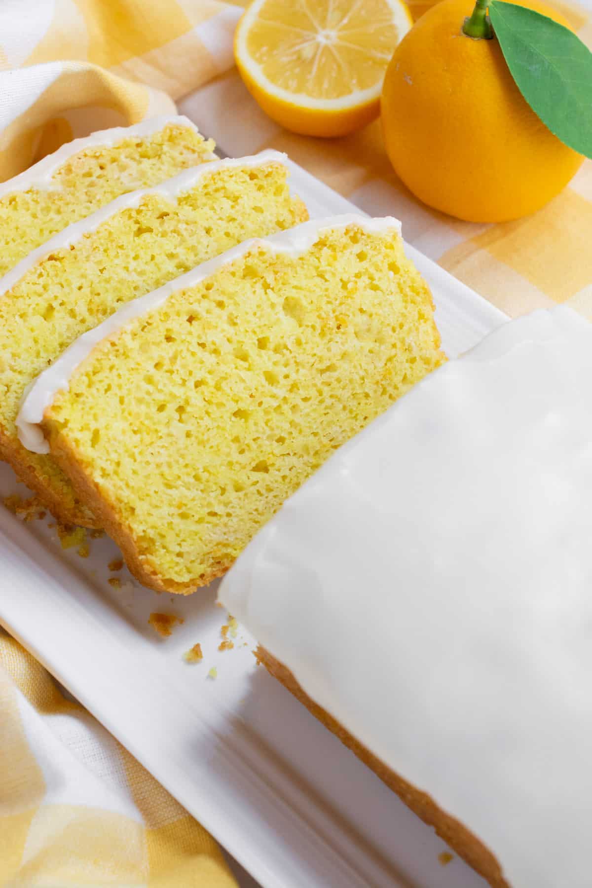 Vegan lemon loaf topped with icing and three slices cut and laying staggered on each other.