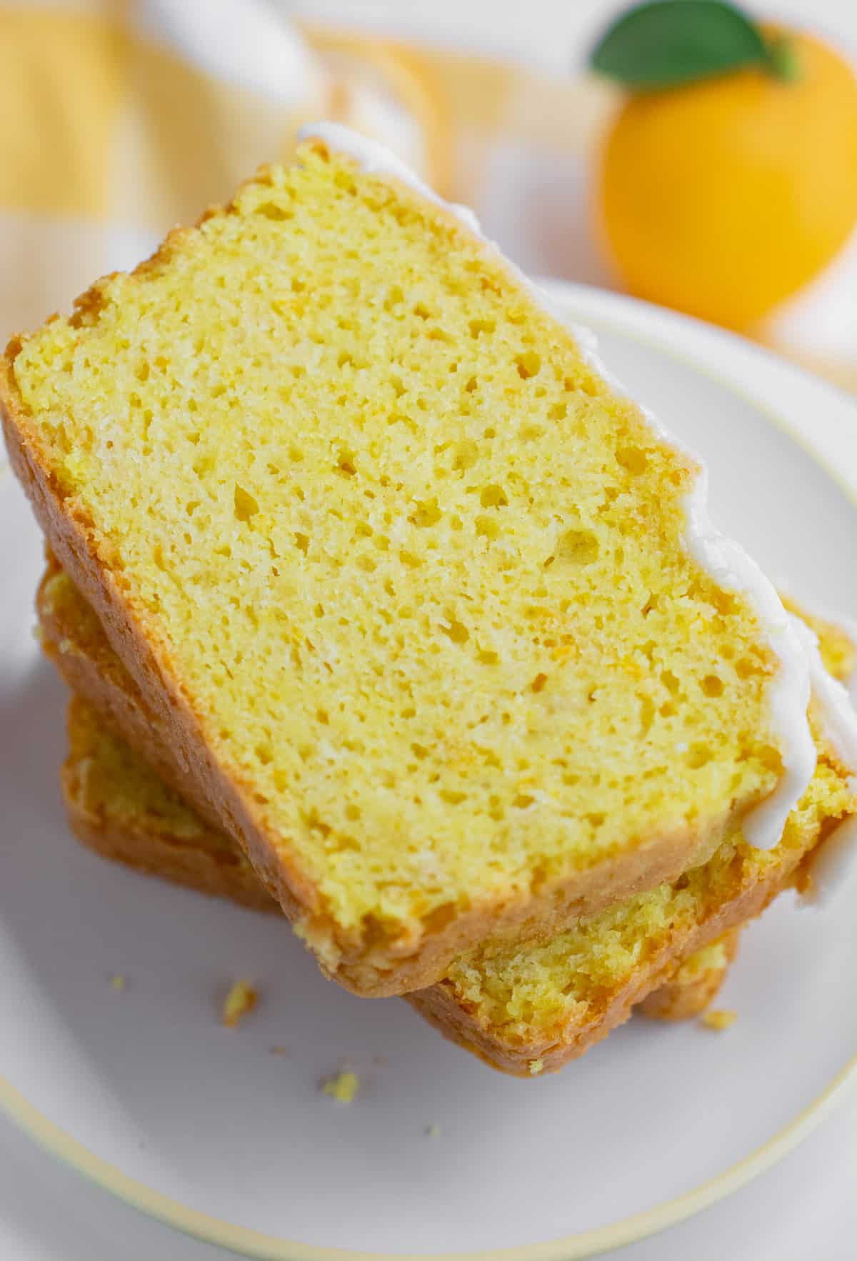 Three slices of vegan lemon bread stacked on top of each other on a white plate with a pale yellow rim.