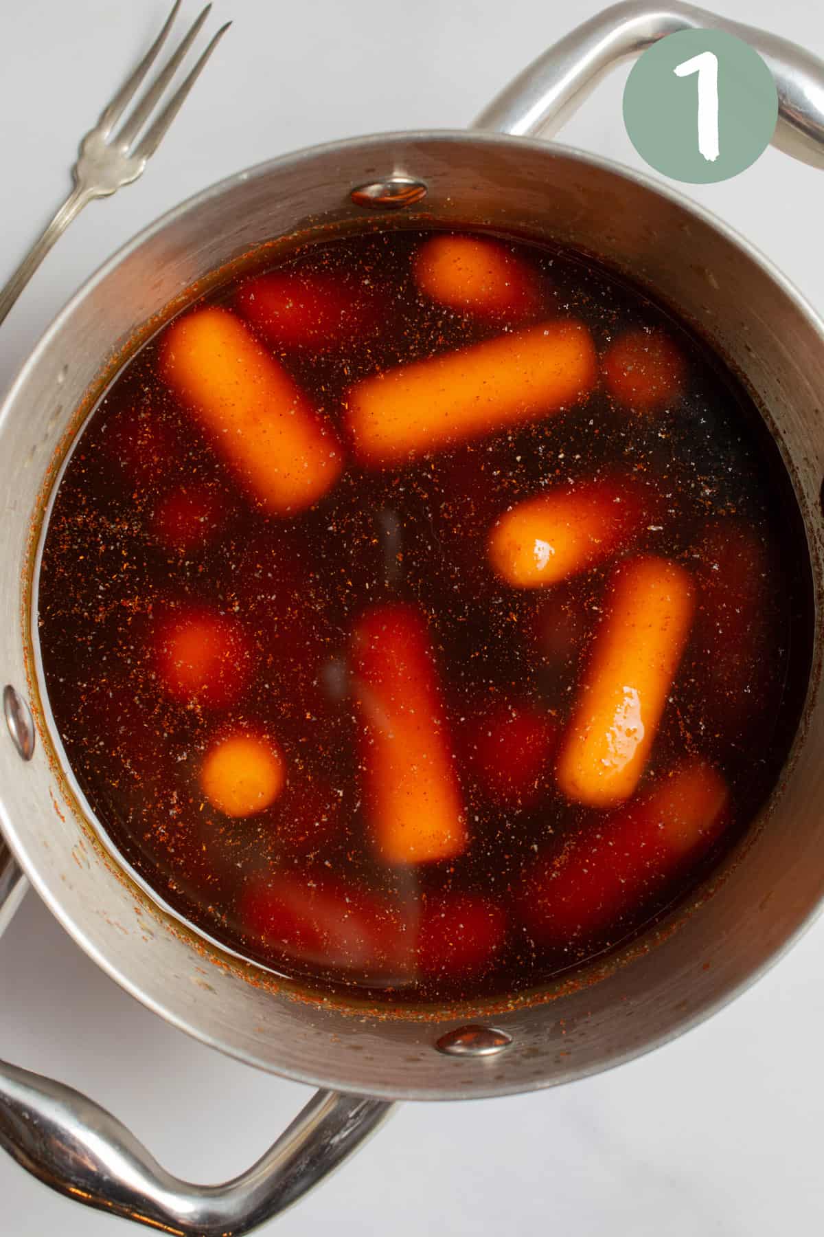 Baby carrots sitting in marinade in a small metal pot with side handles.