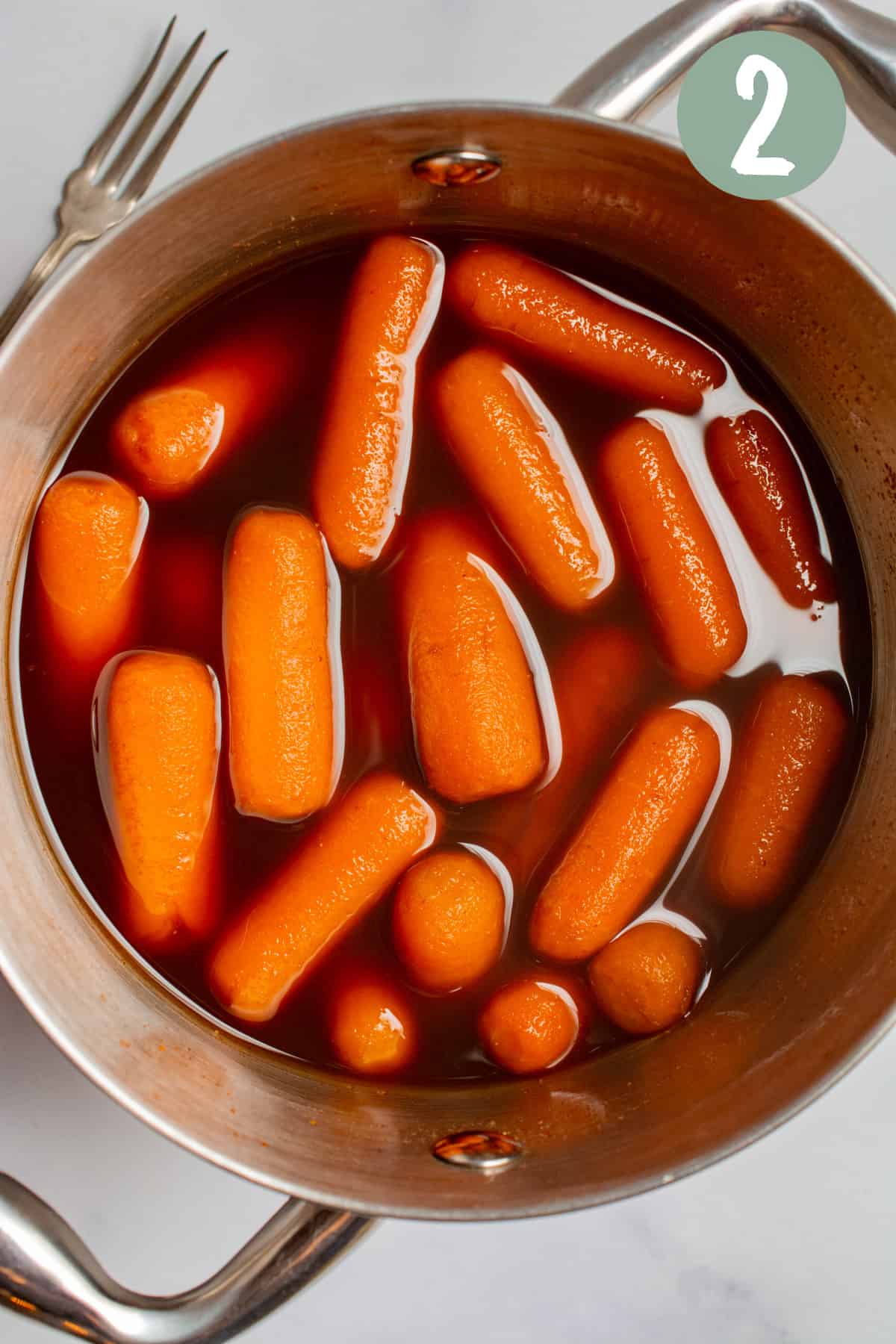 A small metal pot with side handles and baby carrots cooked in marinade in side the pot. 