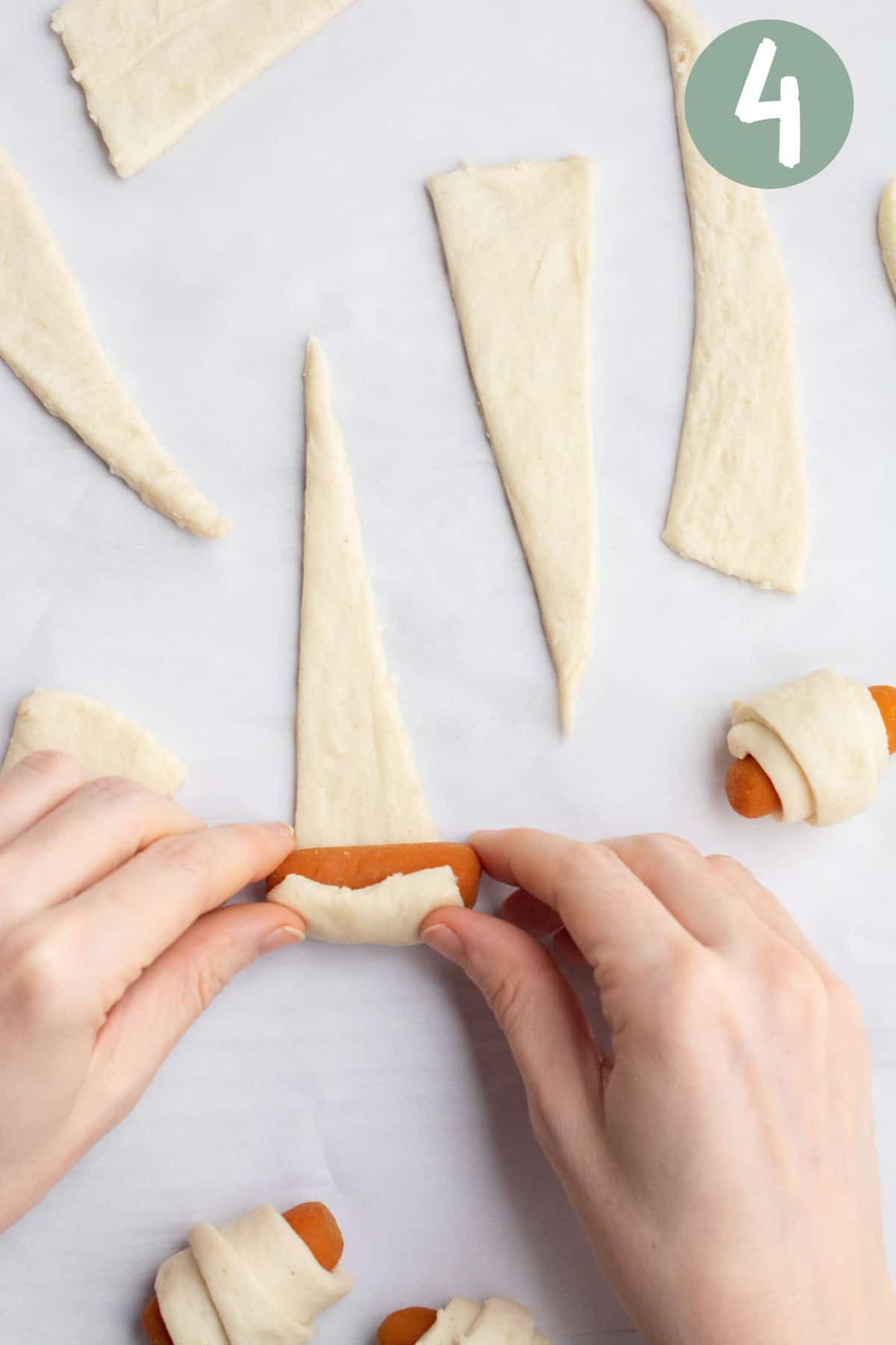 Hands rolling up a marinated carrot in a crescent dough triangle.