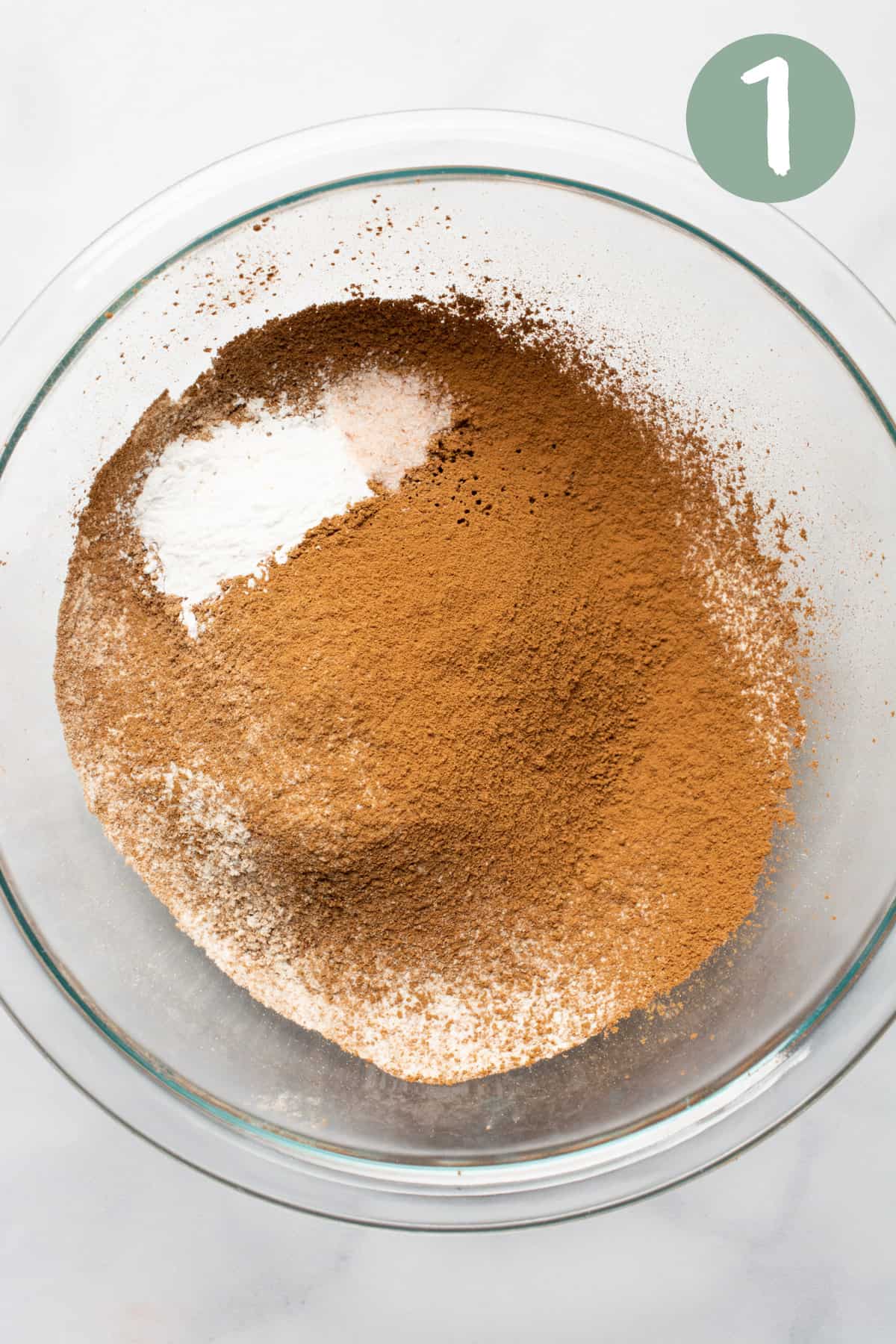 A glass bowl with sifted cocoa powder, flour and baking powder.