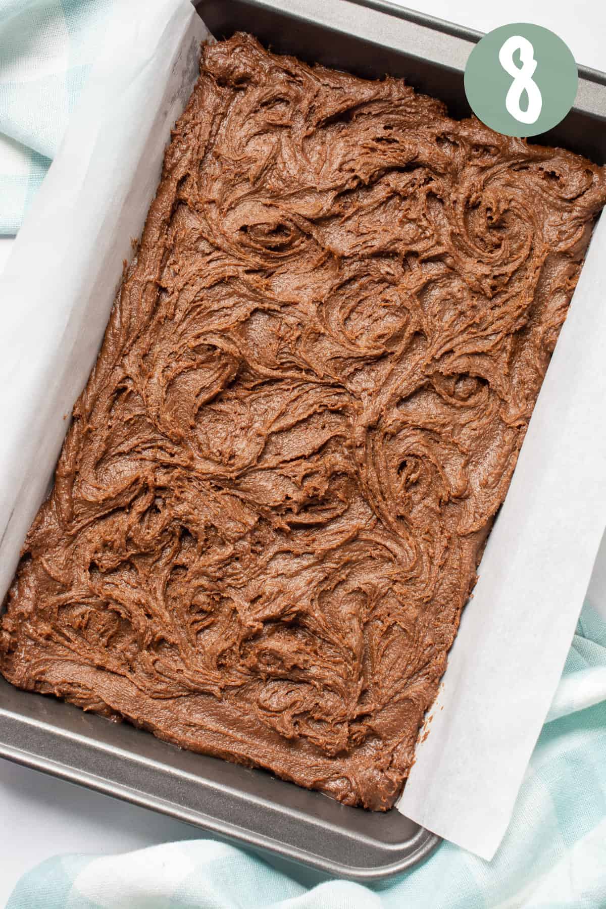 Vegan brownie batter in a 7x11-inch baking pan lined with parchment paper.