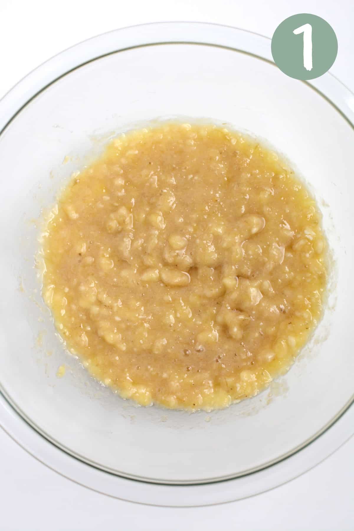 Mashed bananas and oil mixed in a glass bowl.