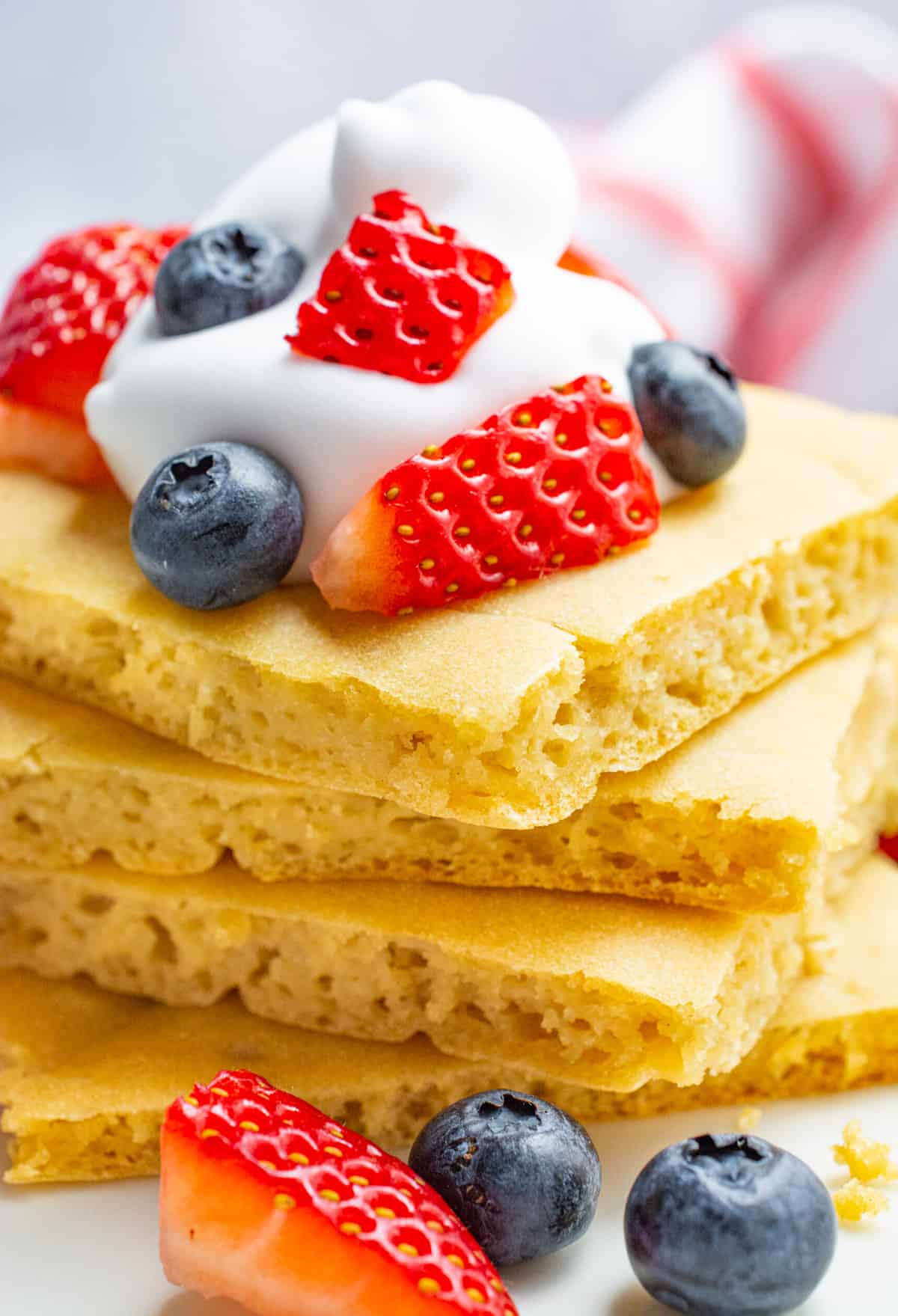 A stack of square pancakes topped with fresh strawberries, blueberries and coconut whip.