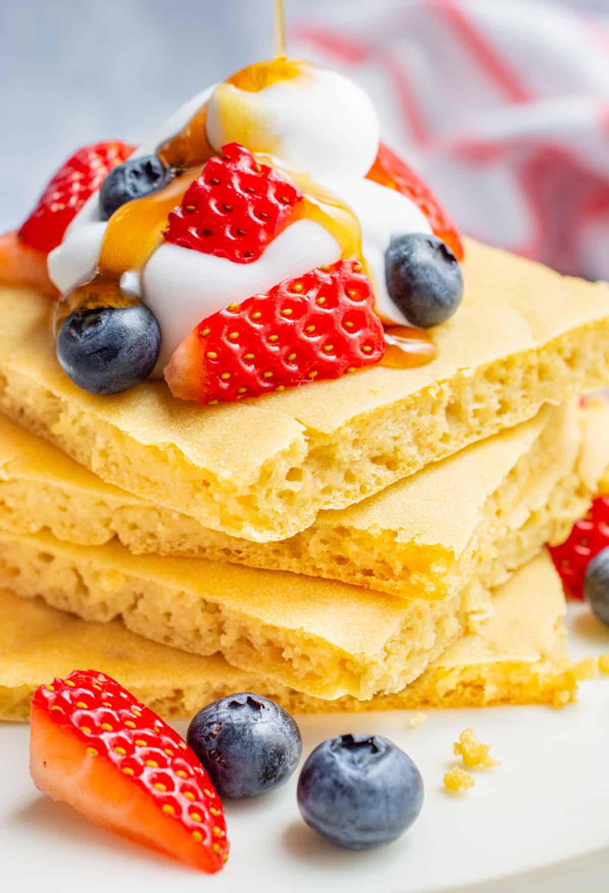 Sheet pan pancakes topped with whip, fruit, and maple syrup drizzling down.