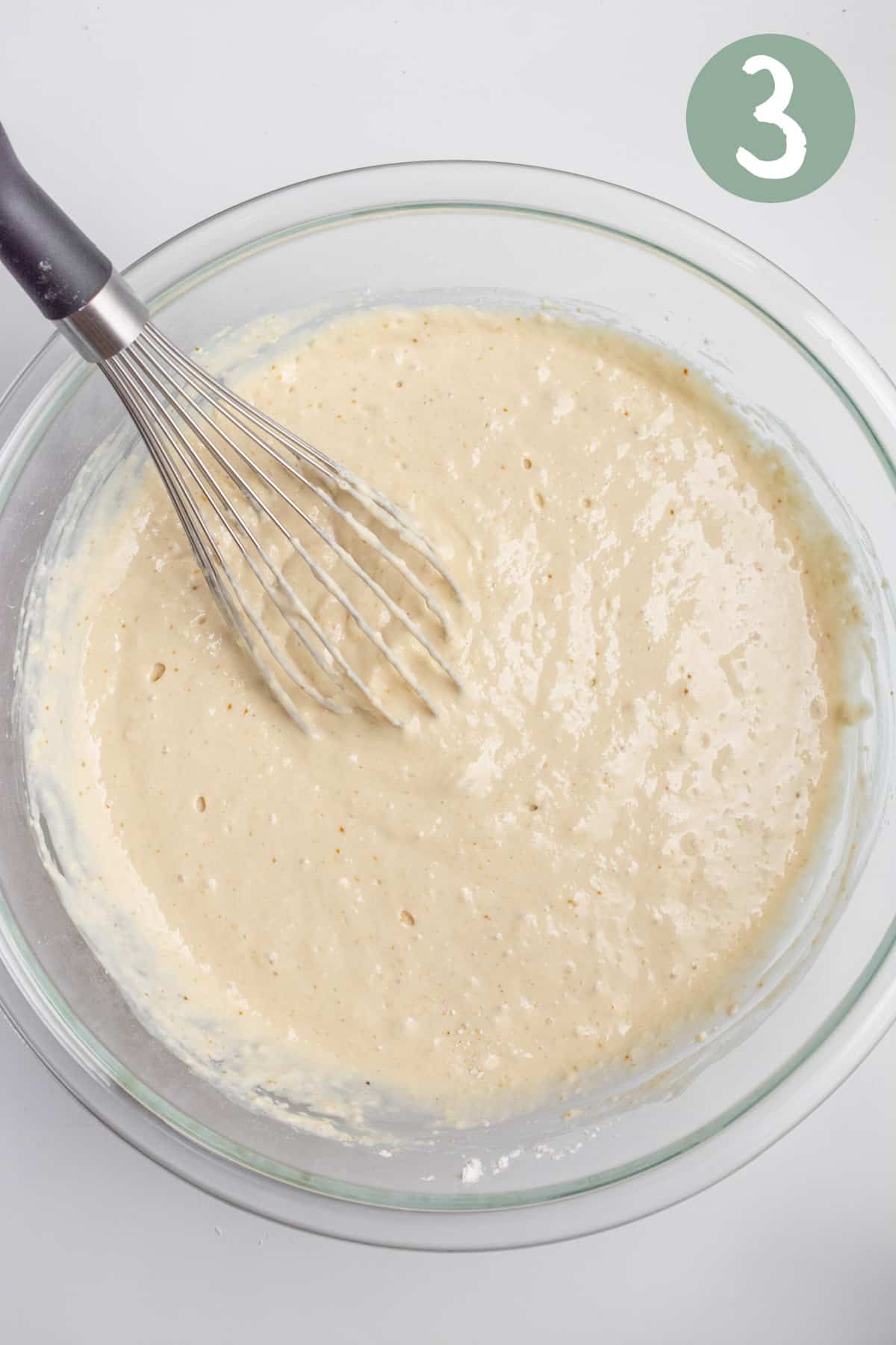 A glass bowl of vegan pancake batter with a whisk.