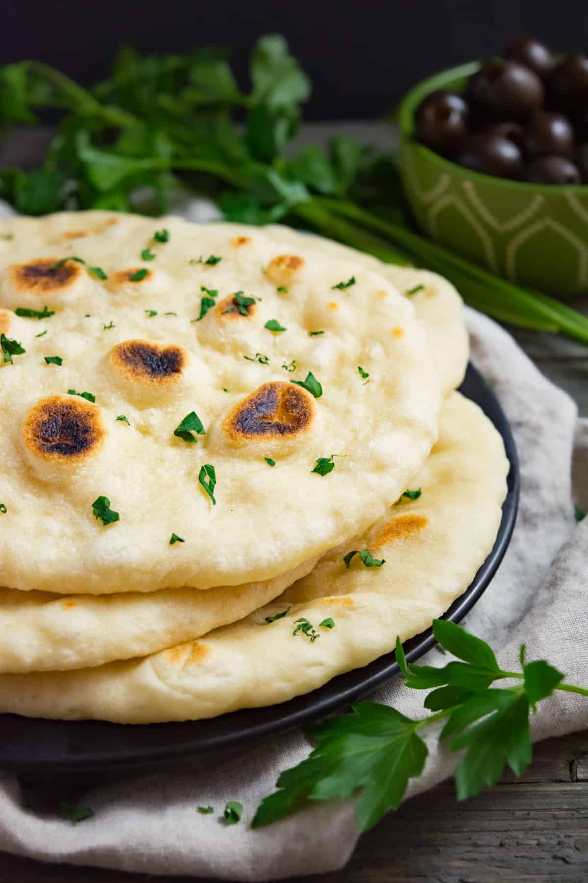 Soft vegan naan bread stacked on a black plate.