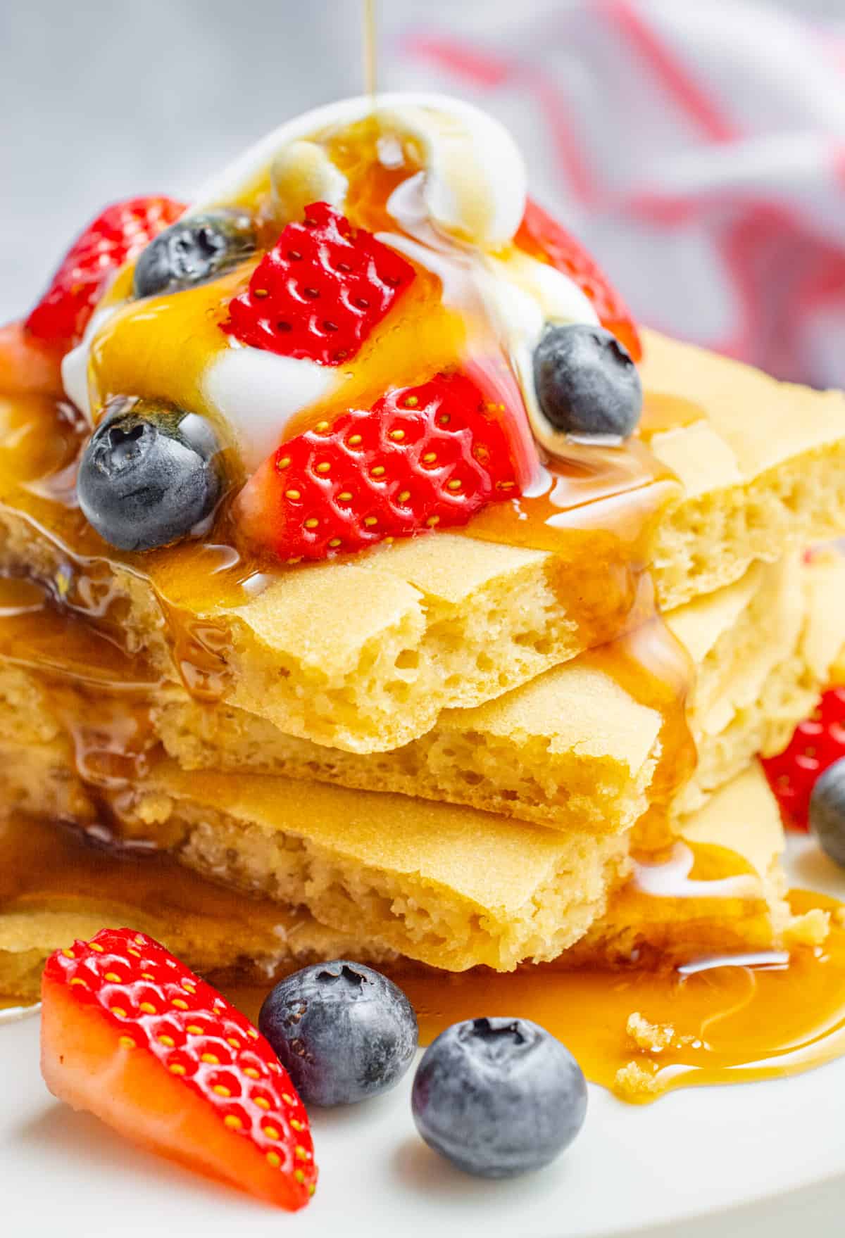 A stack of vegan pancakes topped with fruit, whip and maple syrup.