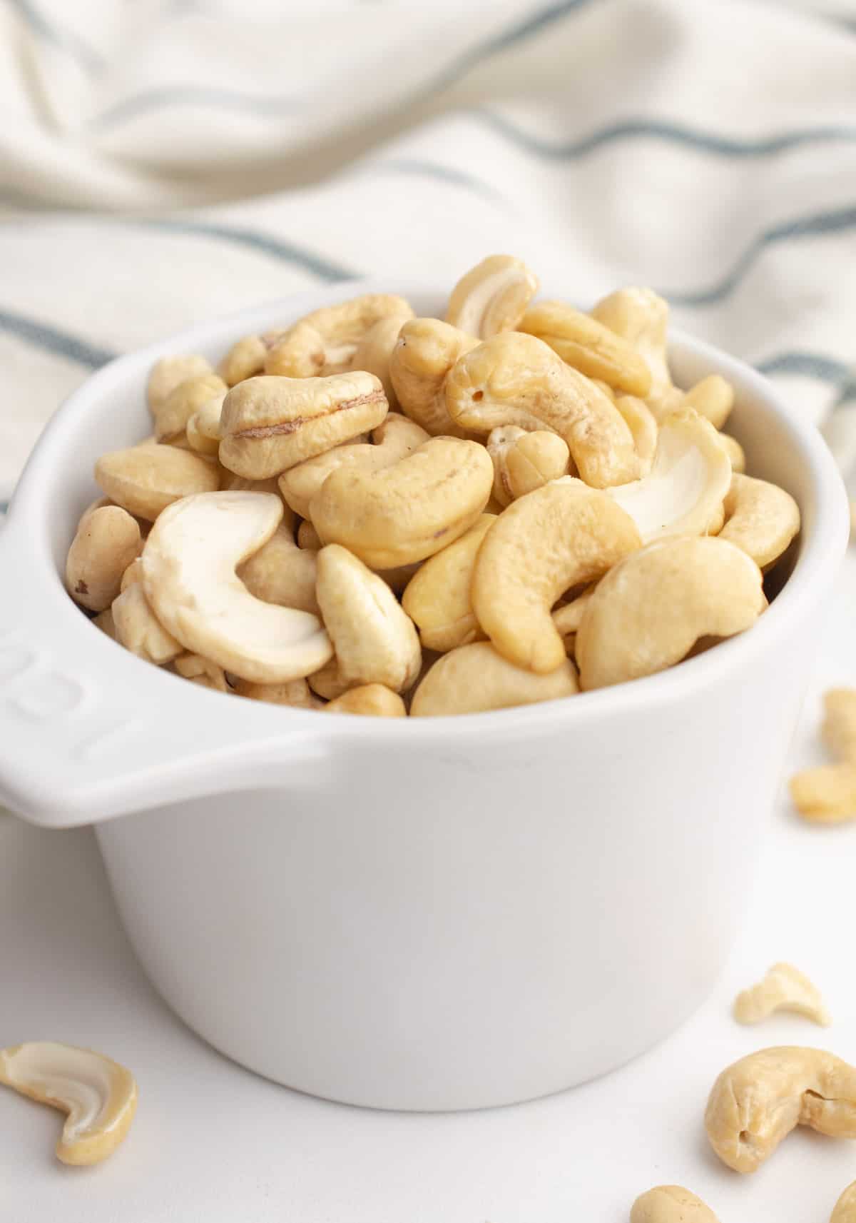 Raw cashews in a white measuring cup.