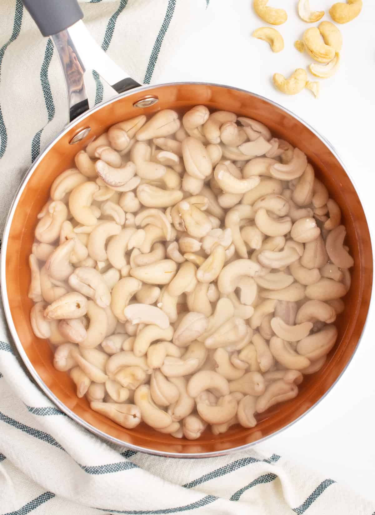 Raw cashews in a pot soaking in hot water.