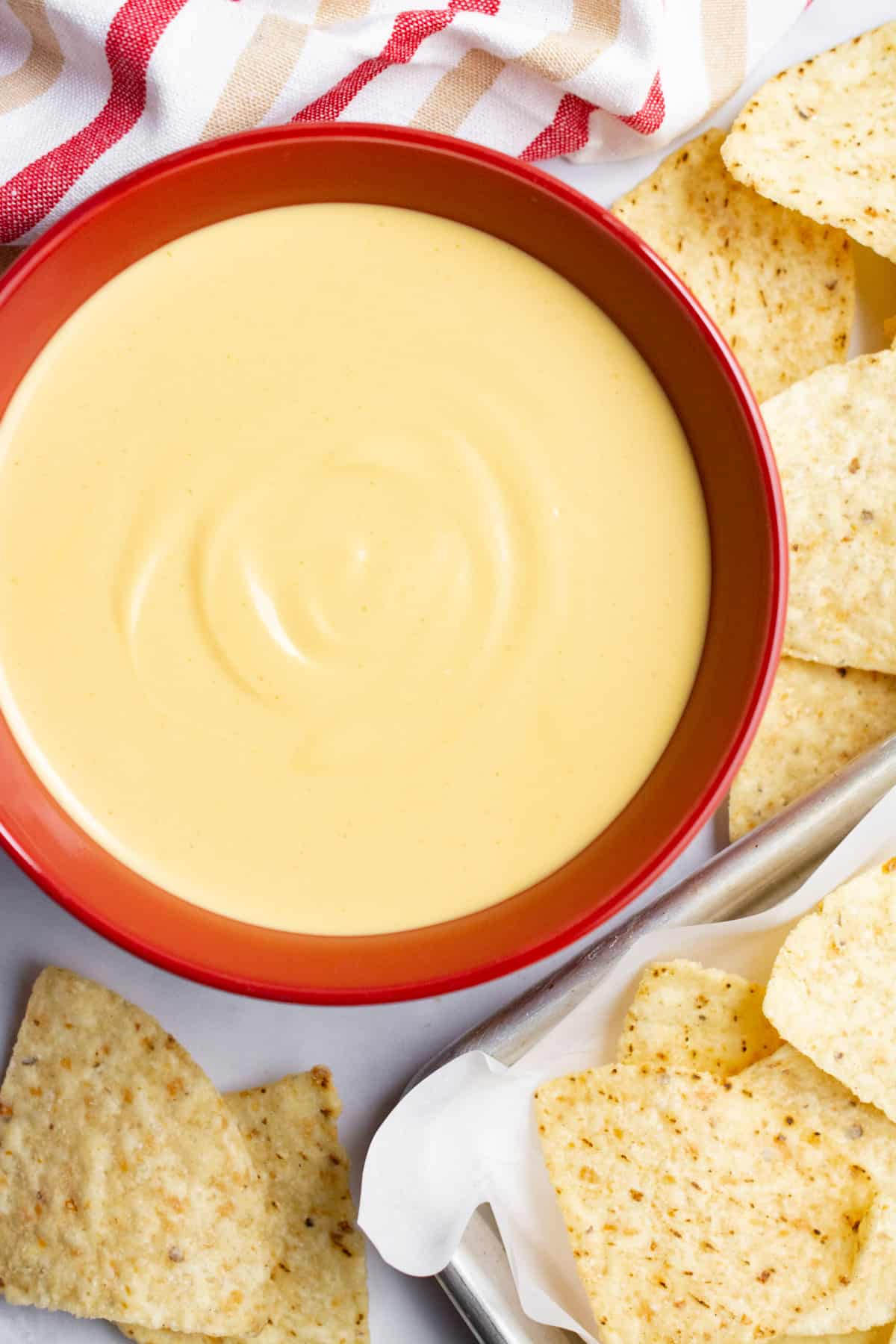 Vegan nacho cheese dip in a red bowl surrounded by tortilla chips