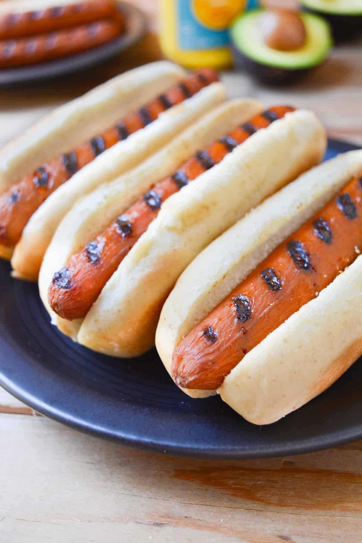 Three carrot hot dogs with charred grill lines in buns.