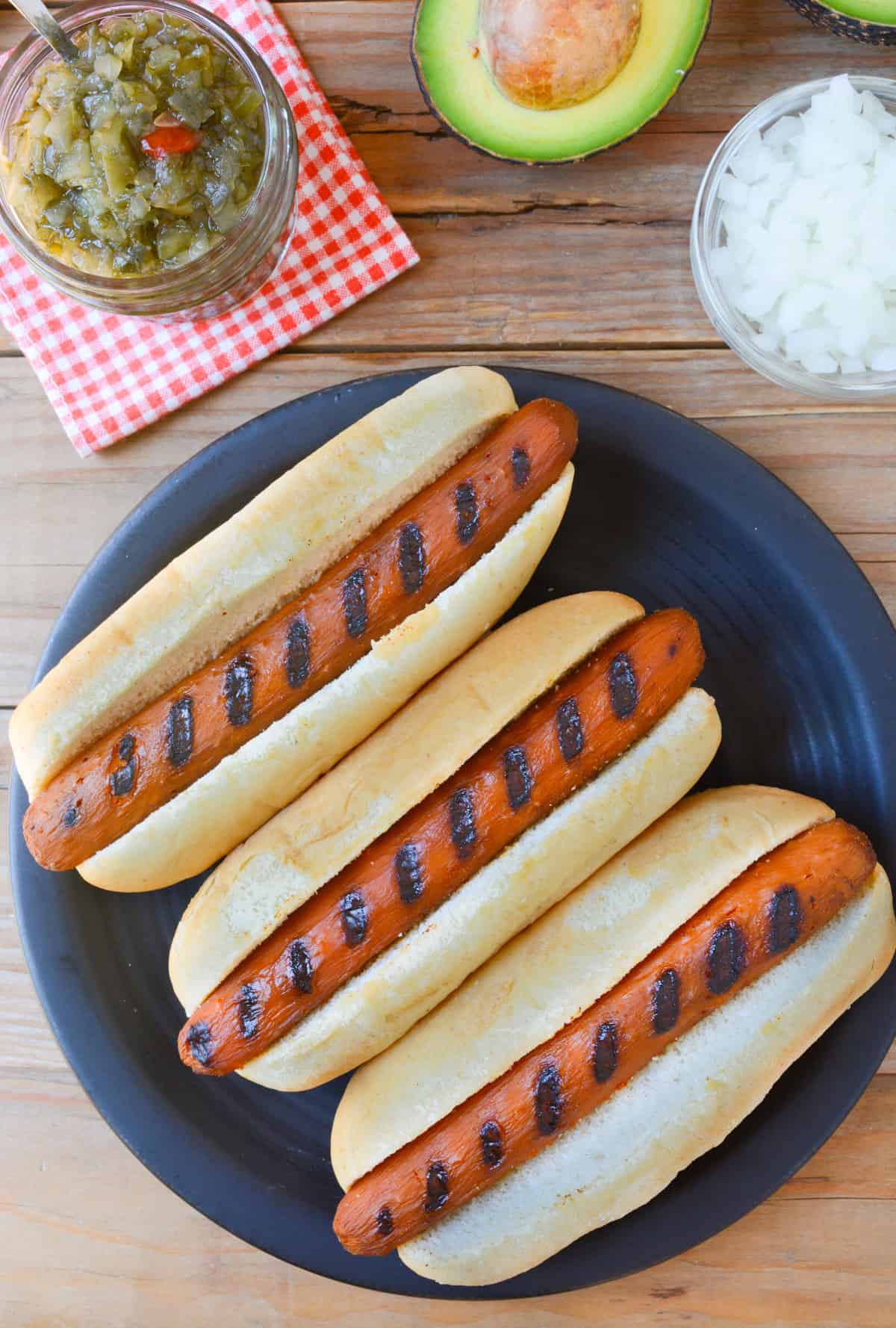 Three carrot hot dogs with grill lines in hot dog buns on a black plate.