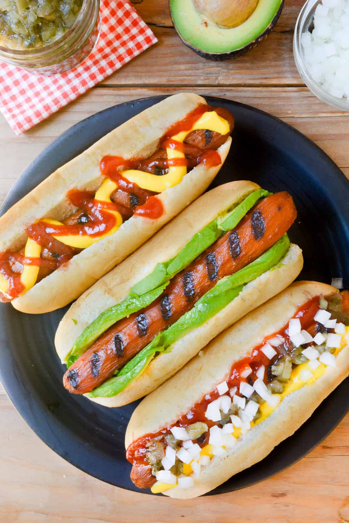 Three carrot dogs with toppings on a black plate.