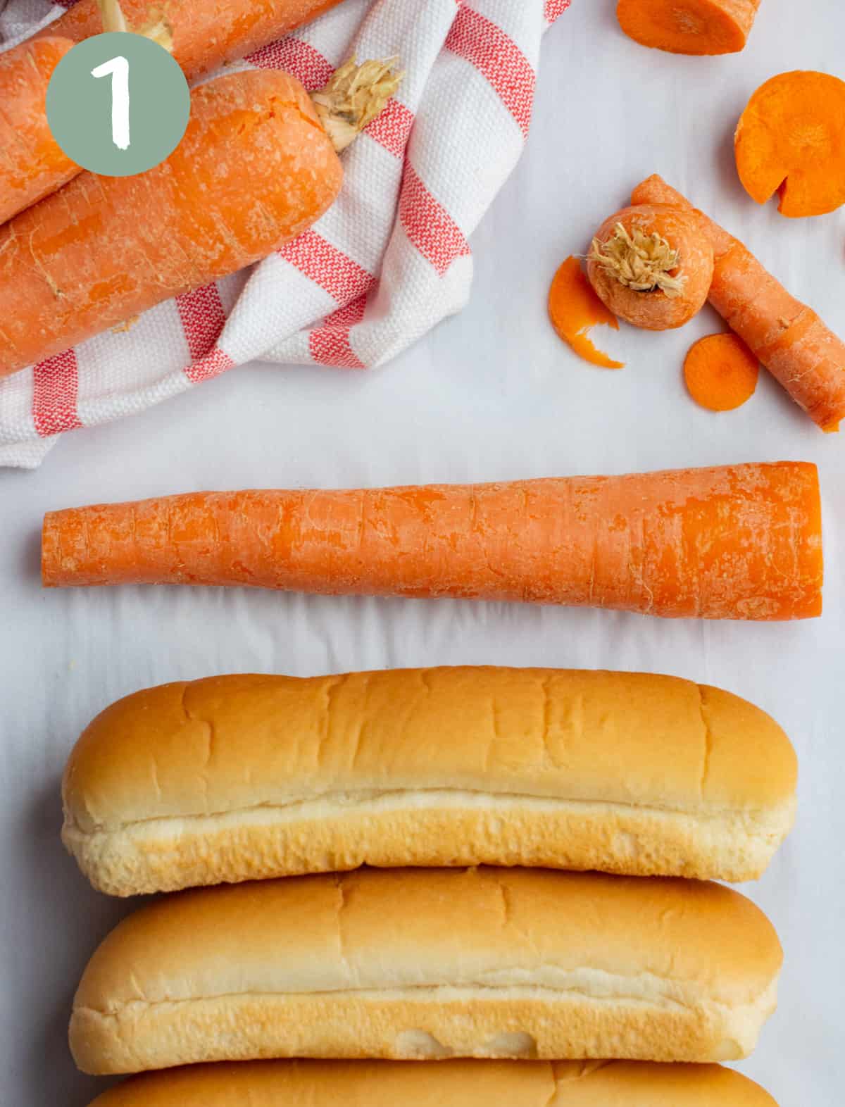 A carrot with both ends cut off next to a hot dog bun showing the length to cut the carrot.