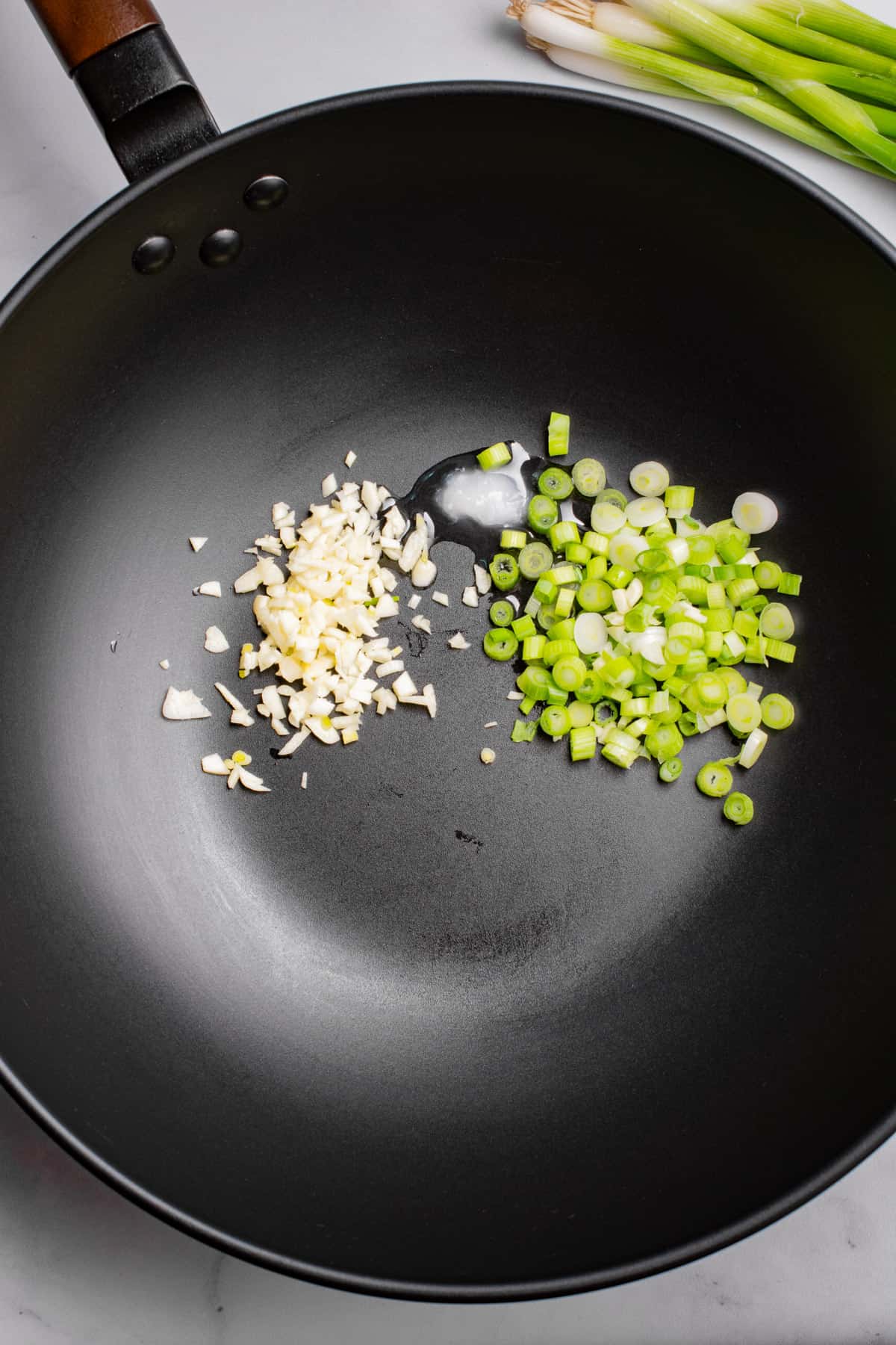 minced garlic, chopped green onion, and oil in a wok.