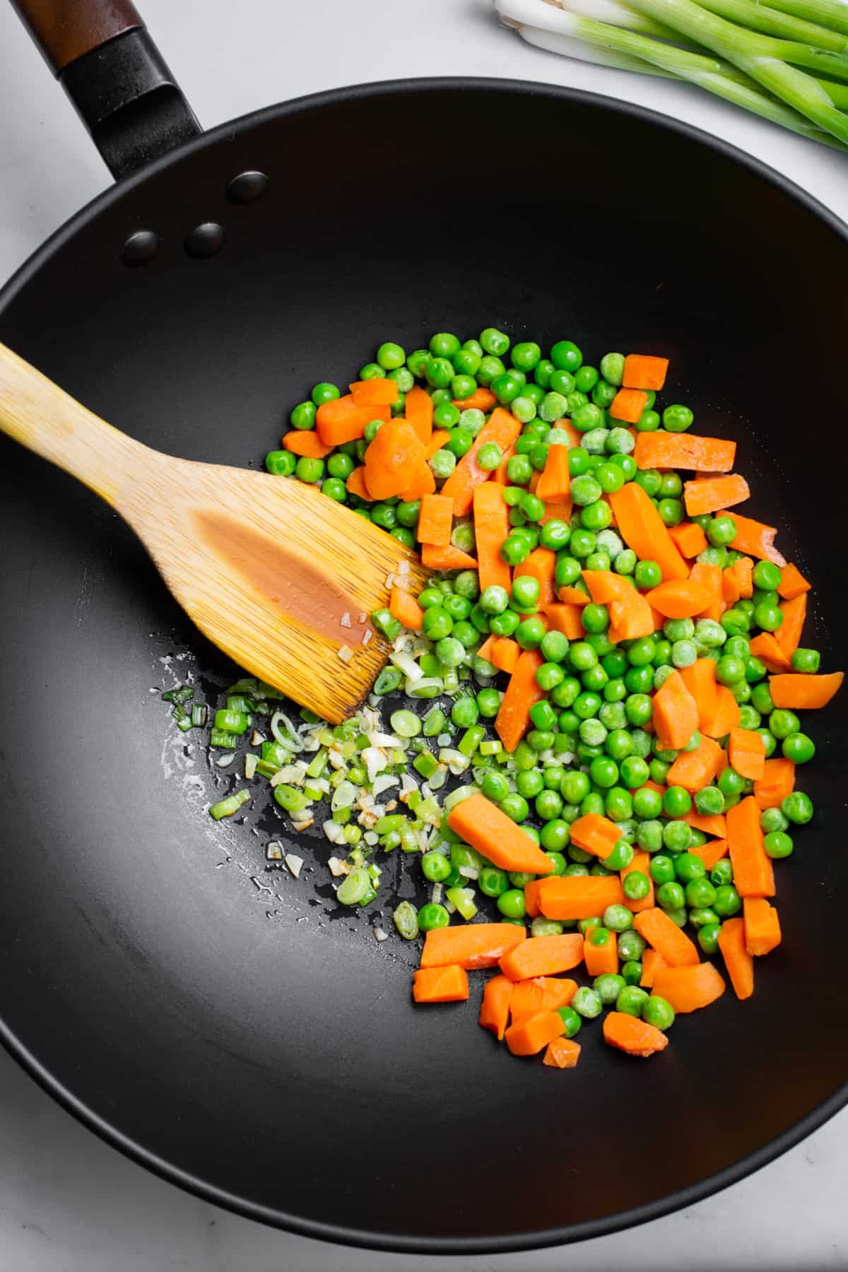 Frozen peas and carrots, garlic, and green onions in a wok.