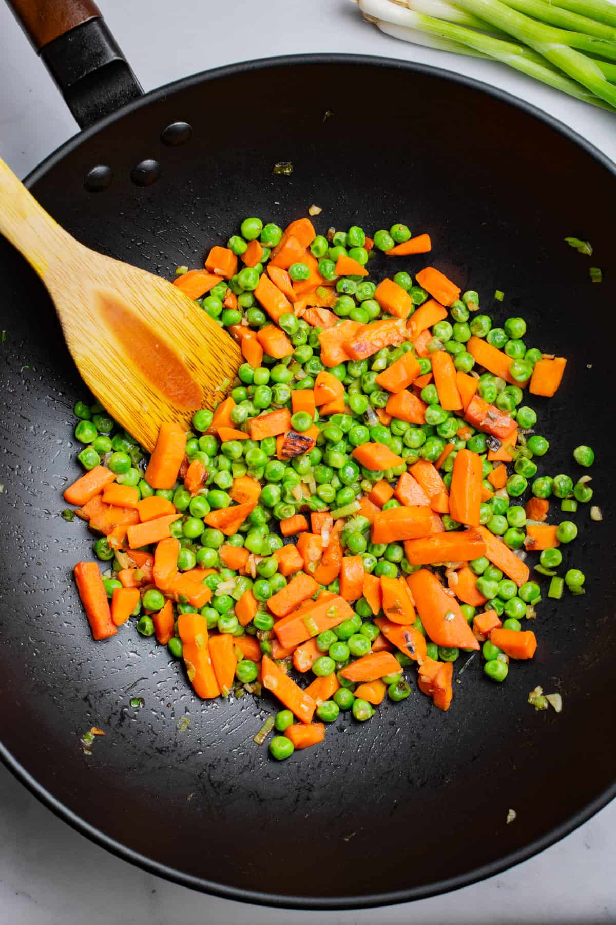 Peas and carrots stir fried in a wok.