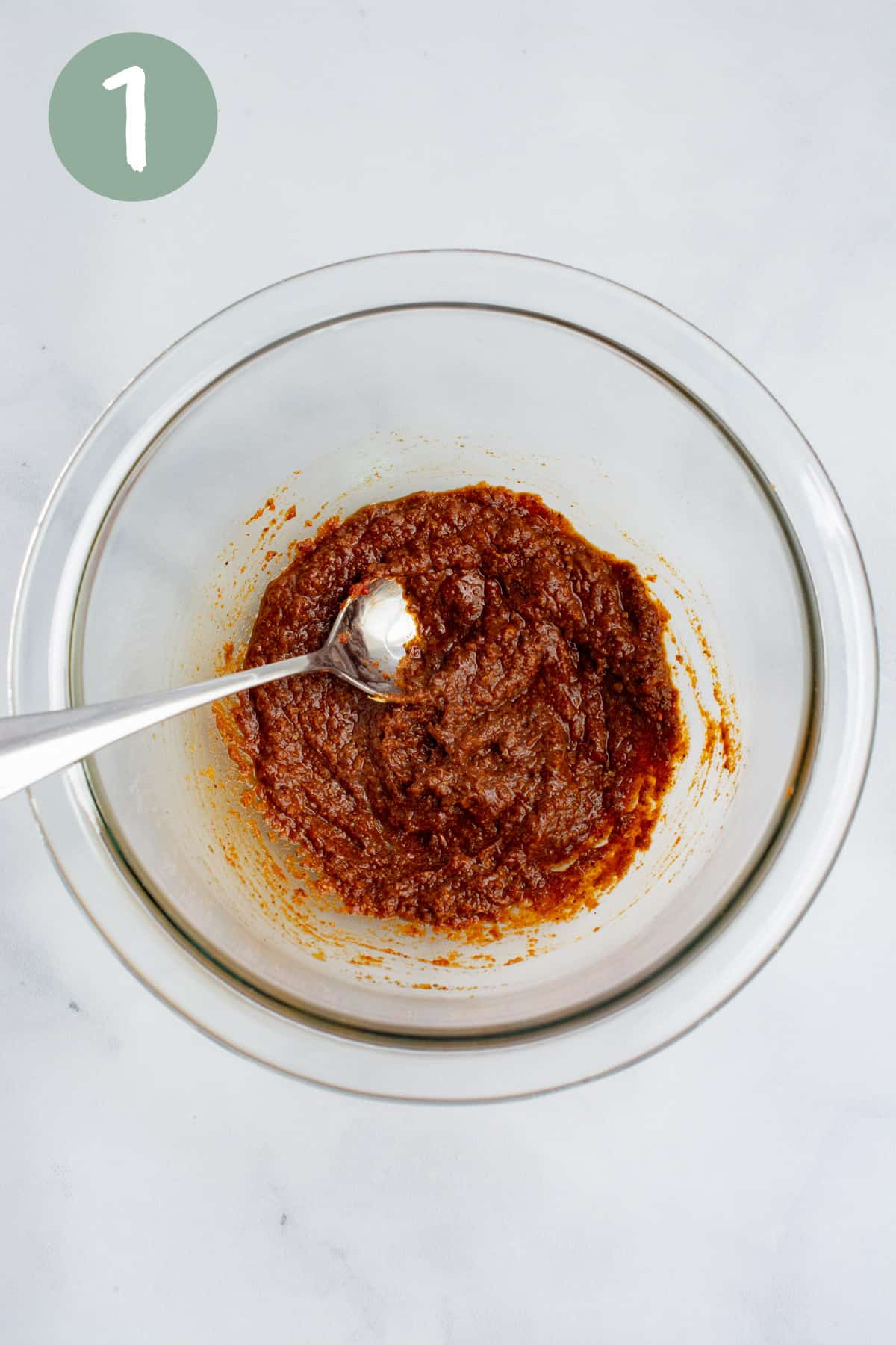 A small glass bowl of tomato paste and seasonings with a spoon.