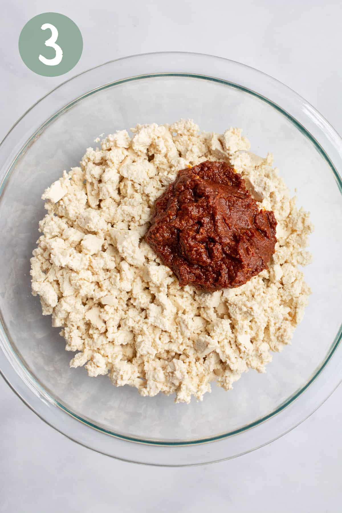 Tofu crumble with a dollop of tomato paste seasonings in a glass bowl.