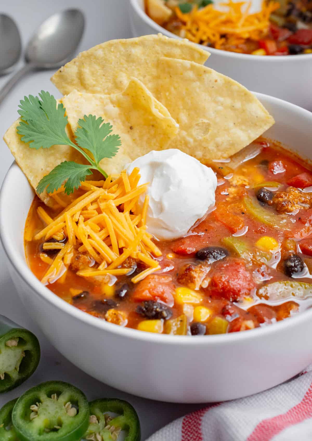 Mexican vegan soup in a white bowl topped with vegan sour cream, vegan cheese, tortilla chips, and fresh cilantro.