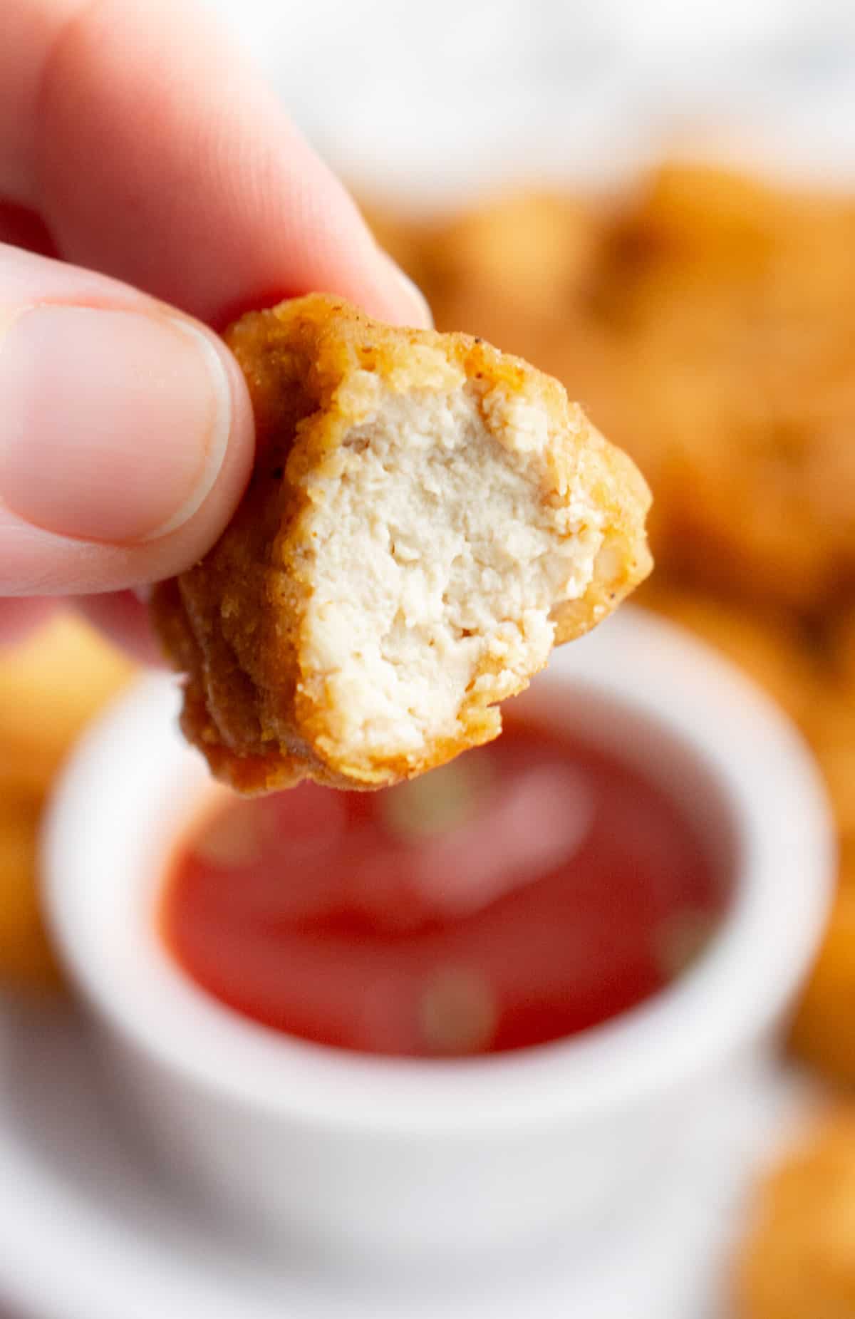 A hand showing the inside of half of a tofu nugget.