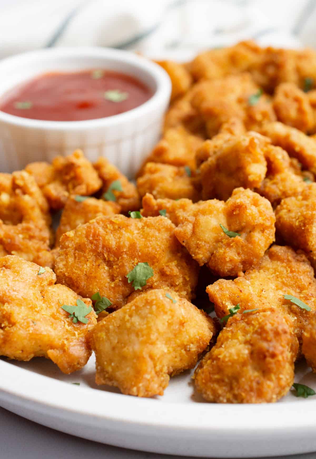 Vegan nuggets on a white plate with a bowl of dipping sauce.