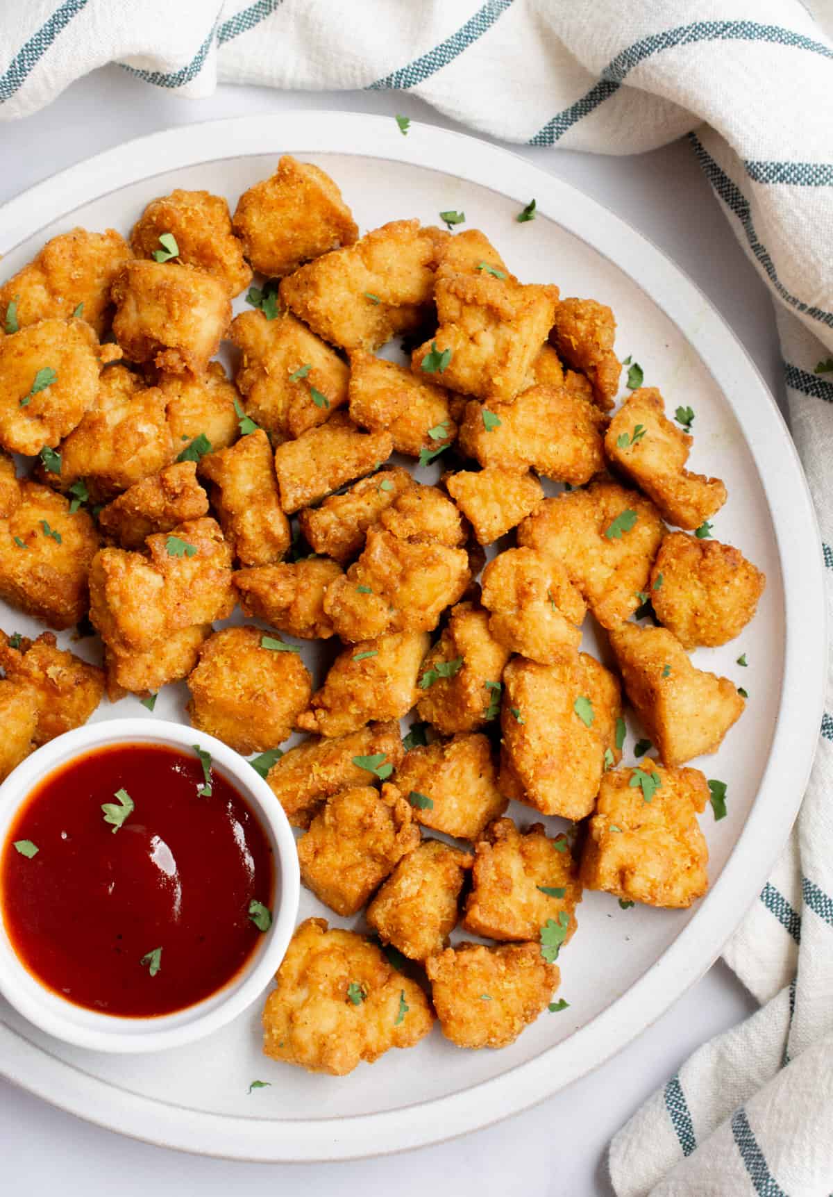 Looking down on a plate of tofu chicken nuggets with a small bowl of BBQ sauce.