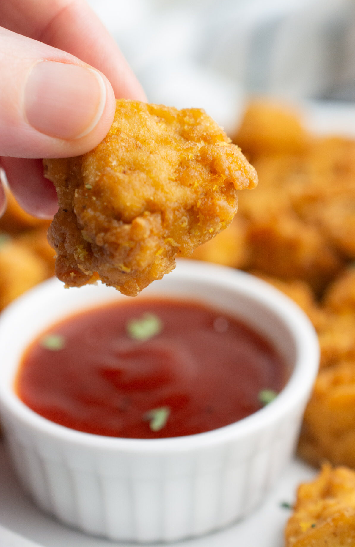 A hand holding a tofu nugget and a bowl of dipping sauce.