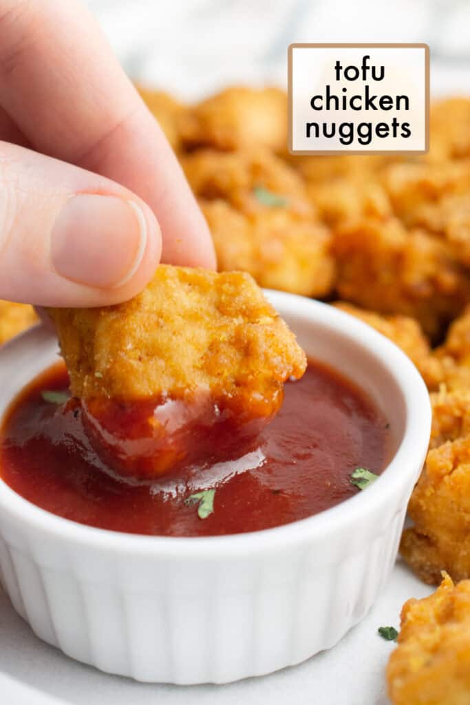 A hand dipping a tofu nugget into bbq sauce.