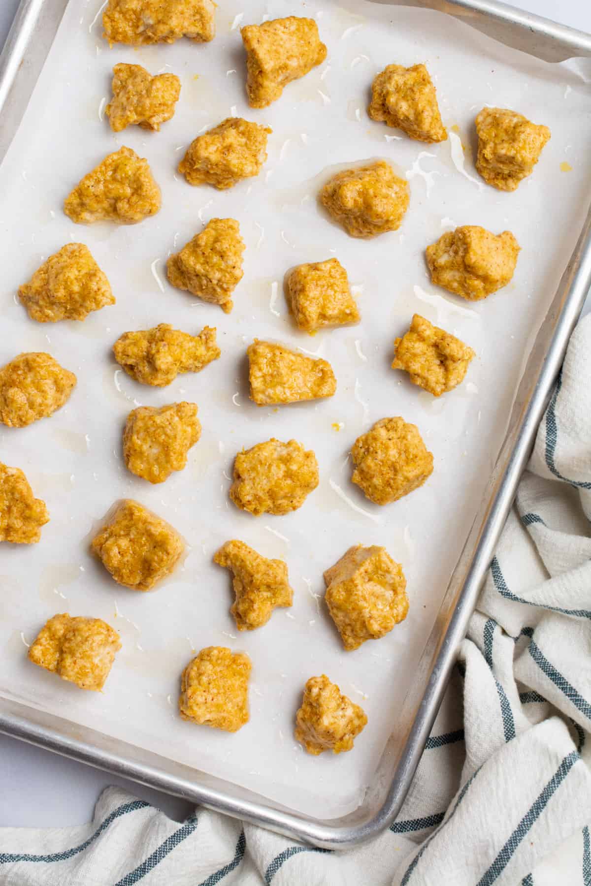 Breaded tofu nuggets on a baking sheet before baking.