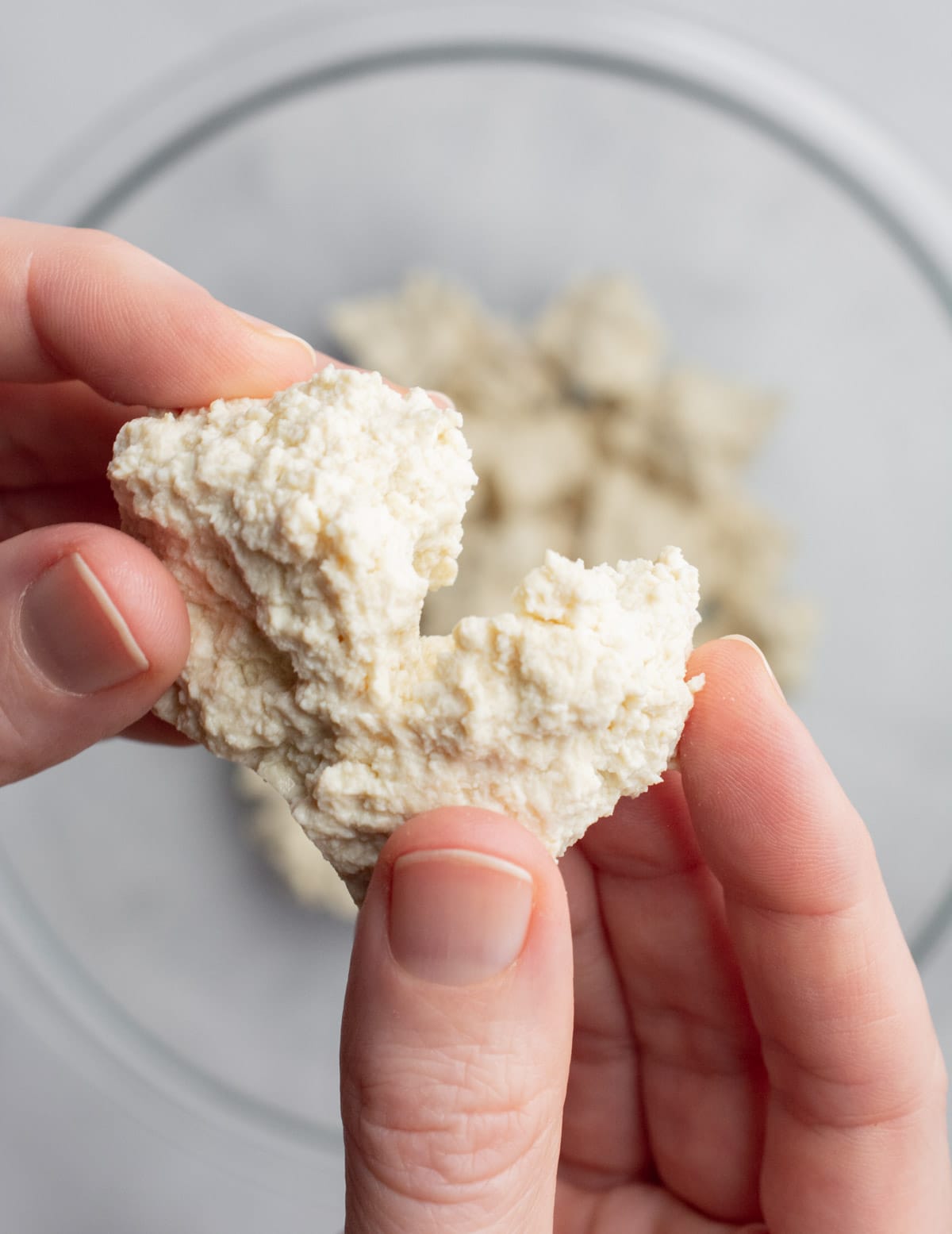 Hands tearing a piece of tofu in half.