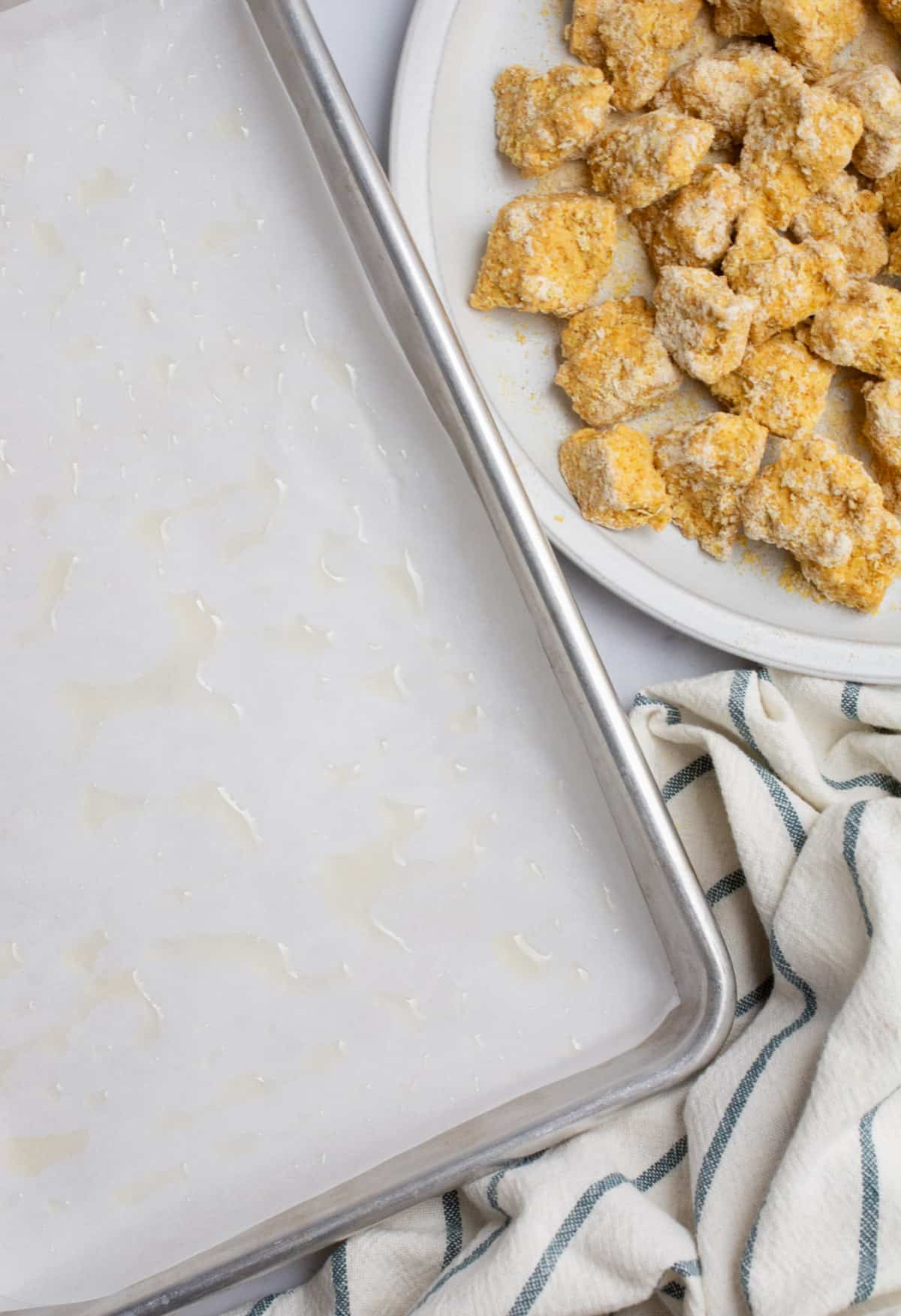 A baking sheet lined with parchment paper and a plate of breaded tofu.