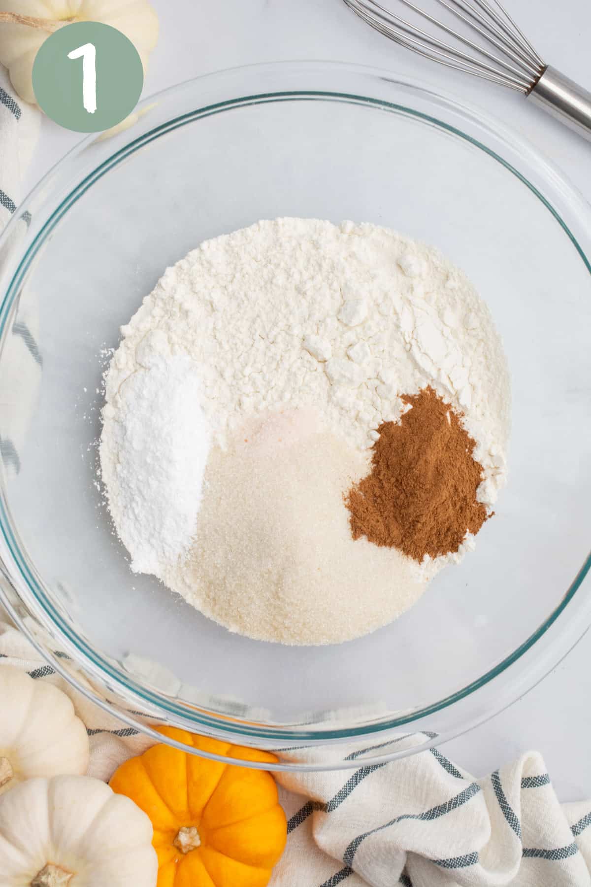 A glass bowl of flour, pumpkin pie spice, sugar, baking powder, and salt.