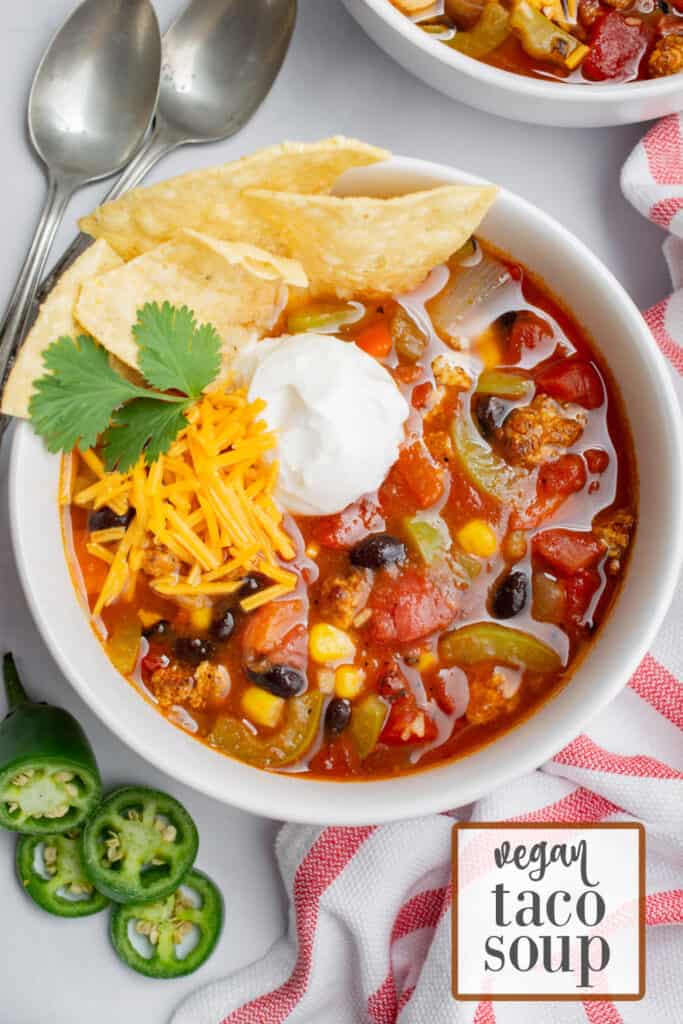 A bowl of vegan taco soup topped with vegan cheese shreds, vegan sour cream, fresh cilantro, and tortilla chips.