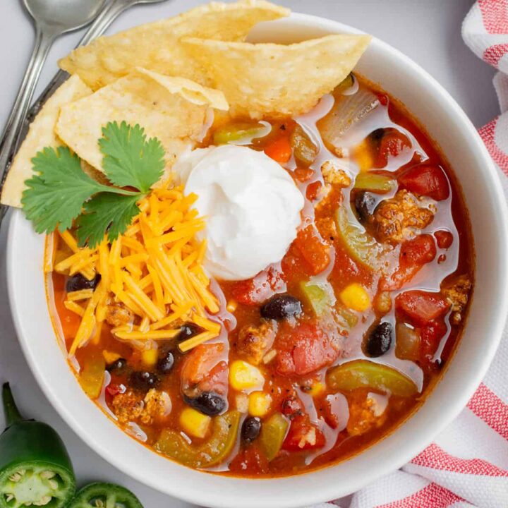 A bowl of vegan taco soup topped with sour cream, vegan cheese, and tortilla chips.