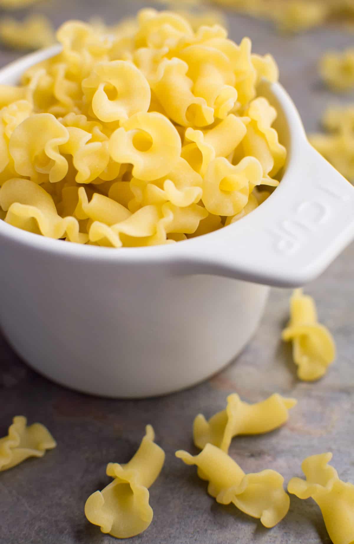A white 1 cup measuring cup full of campanelle pasta.
